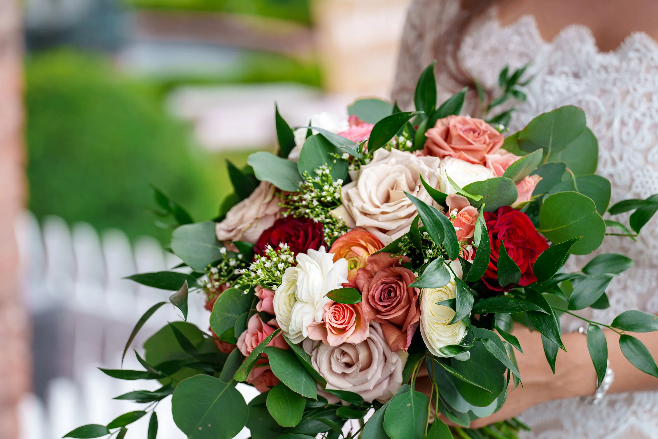 Bride holding a colorful rose bouquet with greenery.