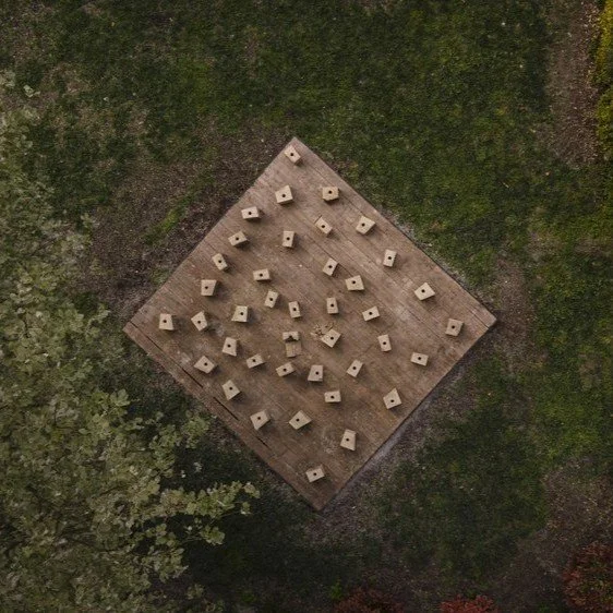 Mosaico de pequeñas esculturas de piedra dispuestas en una base de madera, rodeada de vegetación.