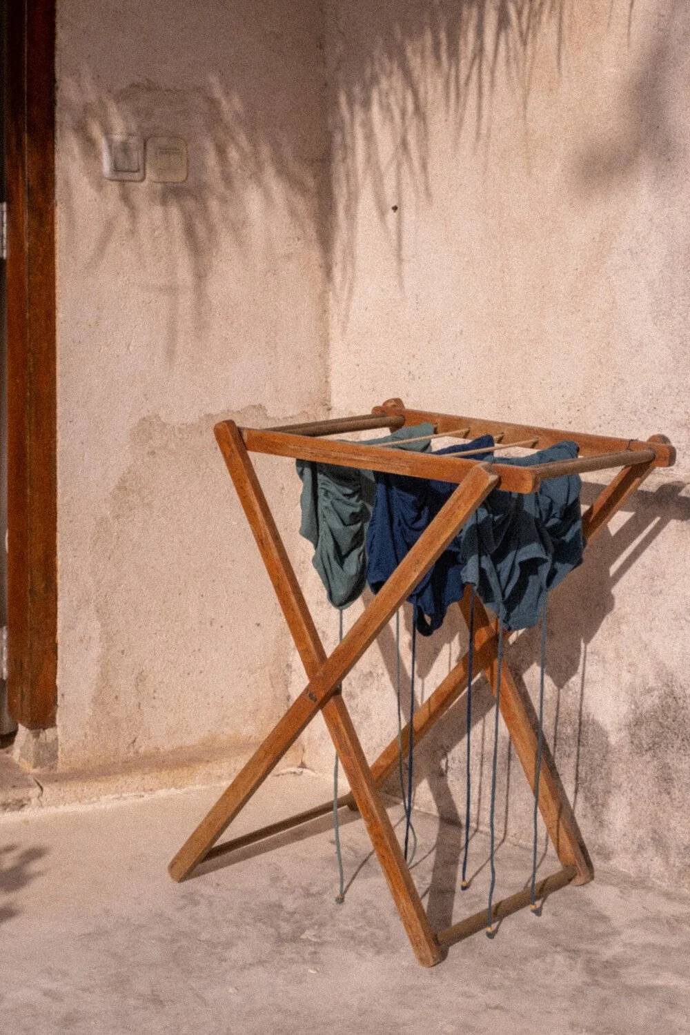 Tendedero de madera con ropa colgada, situado en una pared de color beige con manchas y textura rugosa.