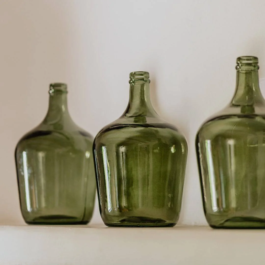 Tres botellas de vidrio verde sobre una repisa blanca