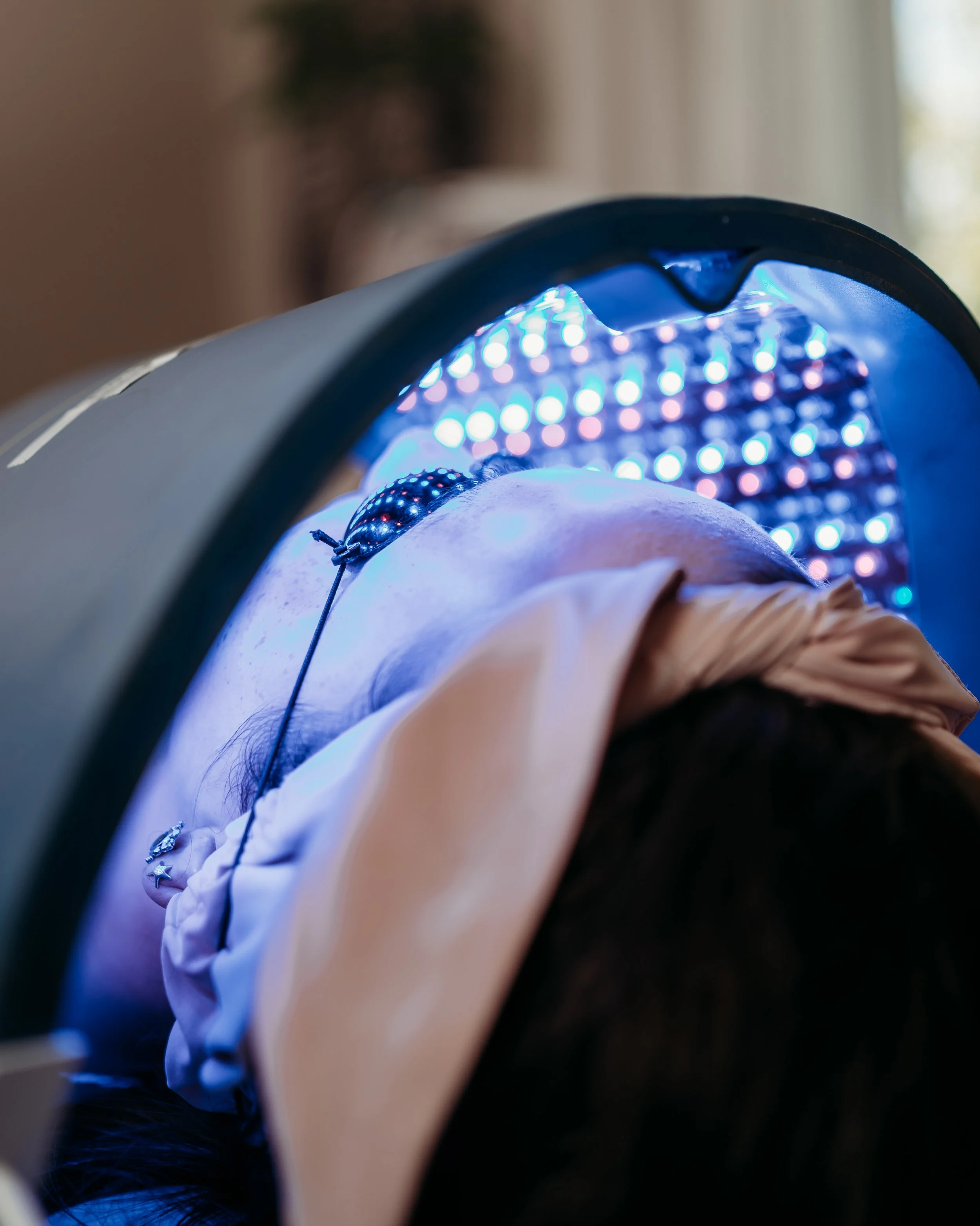 Client relaxing under professional LED light during a facial treatment.