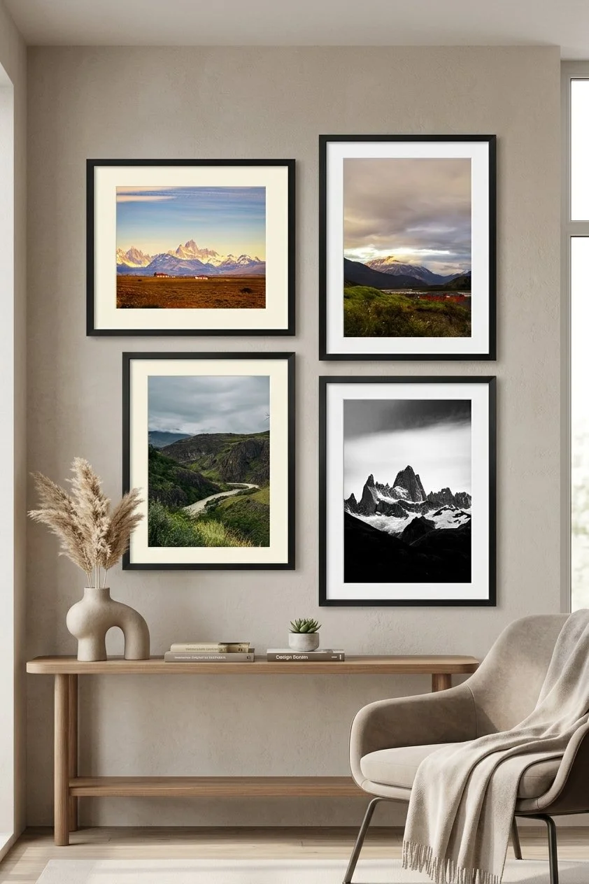 A living room wall with four framed landscape photos of mountains and nature, a wooden console table with decorative items, and a beige armchair with a throw blanket.
