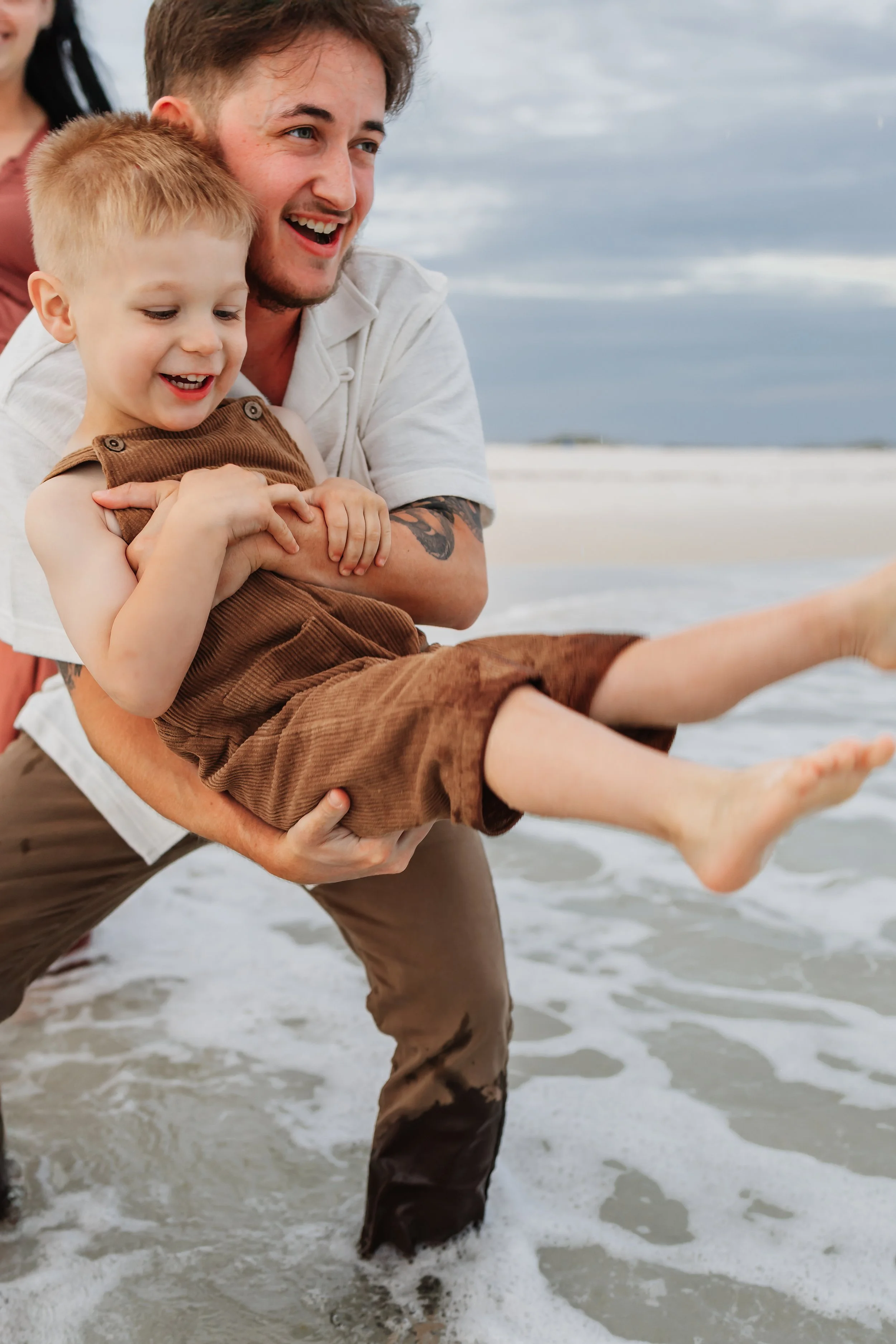 Dad swings young son over the water of the Gulf of America during a session with a Navarre Beach Family Photographer