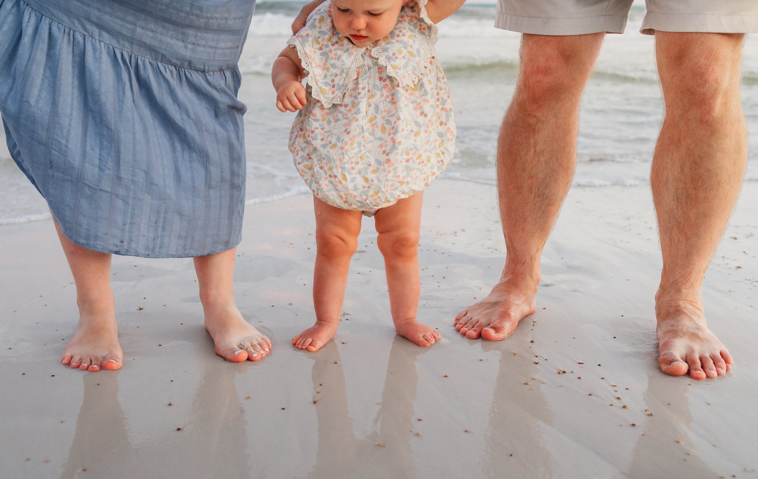 Family of three dipping their toes into the Gulf of America while on vacation at Pensacola Beach.
