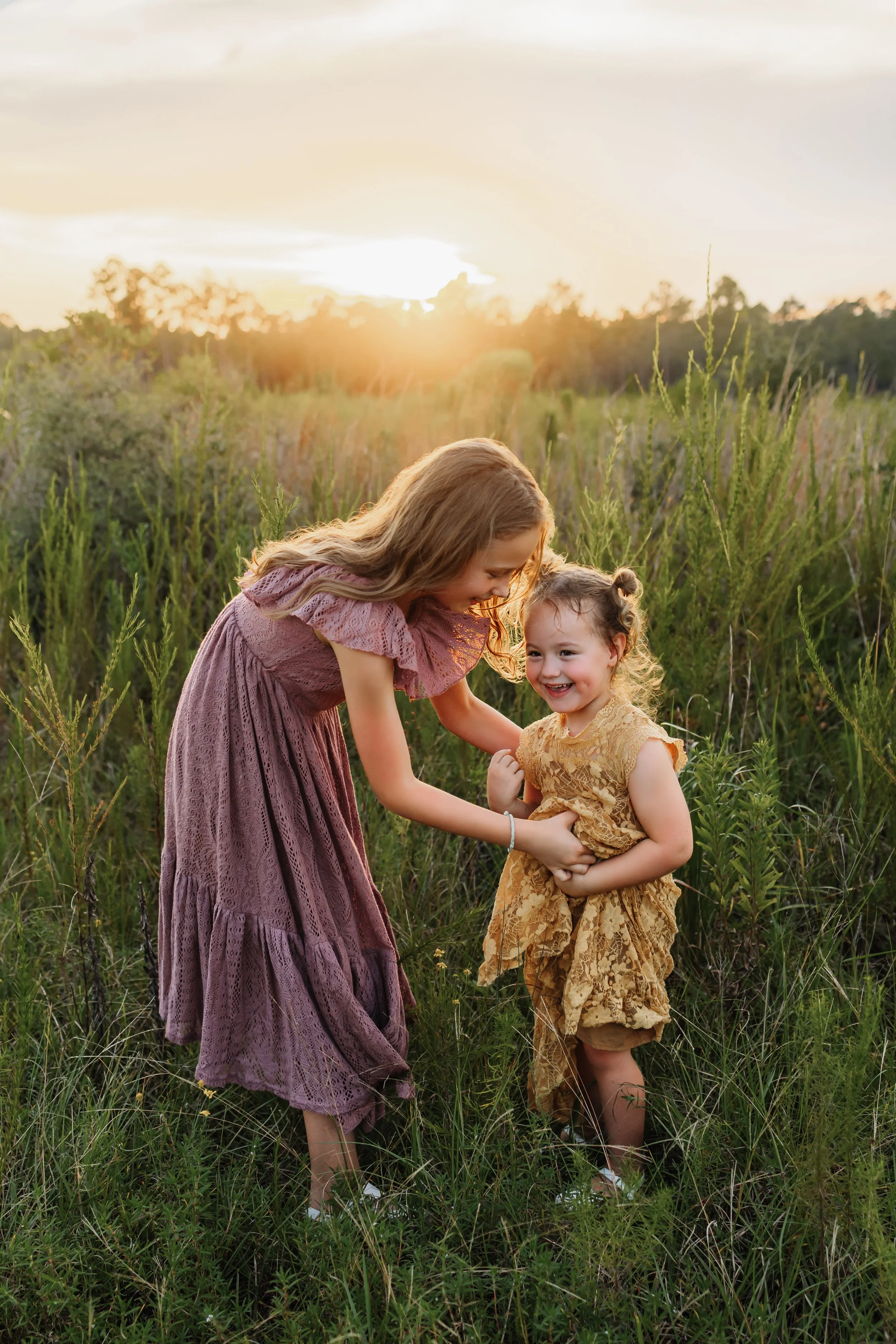 Older sister tickling her little sister in a field near pensacola, FL with Kristen Coberly Photography