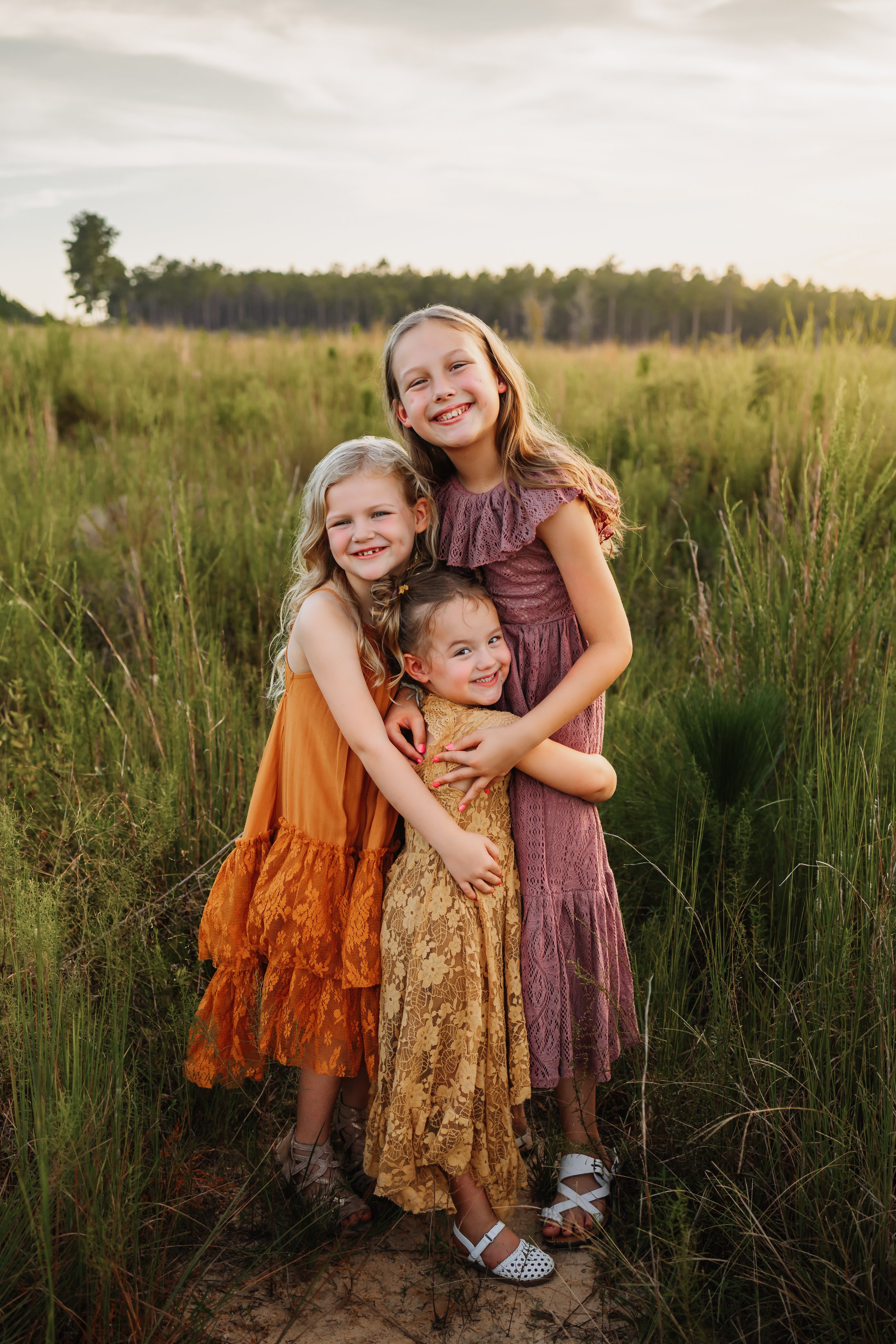 Three sisters hugging in a field near Pensacola, FL during a session with Kristen Coberly Photography