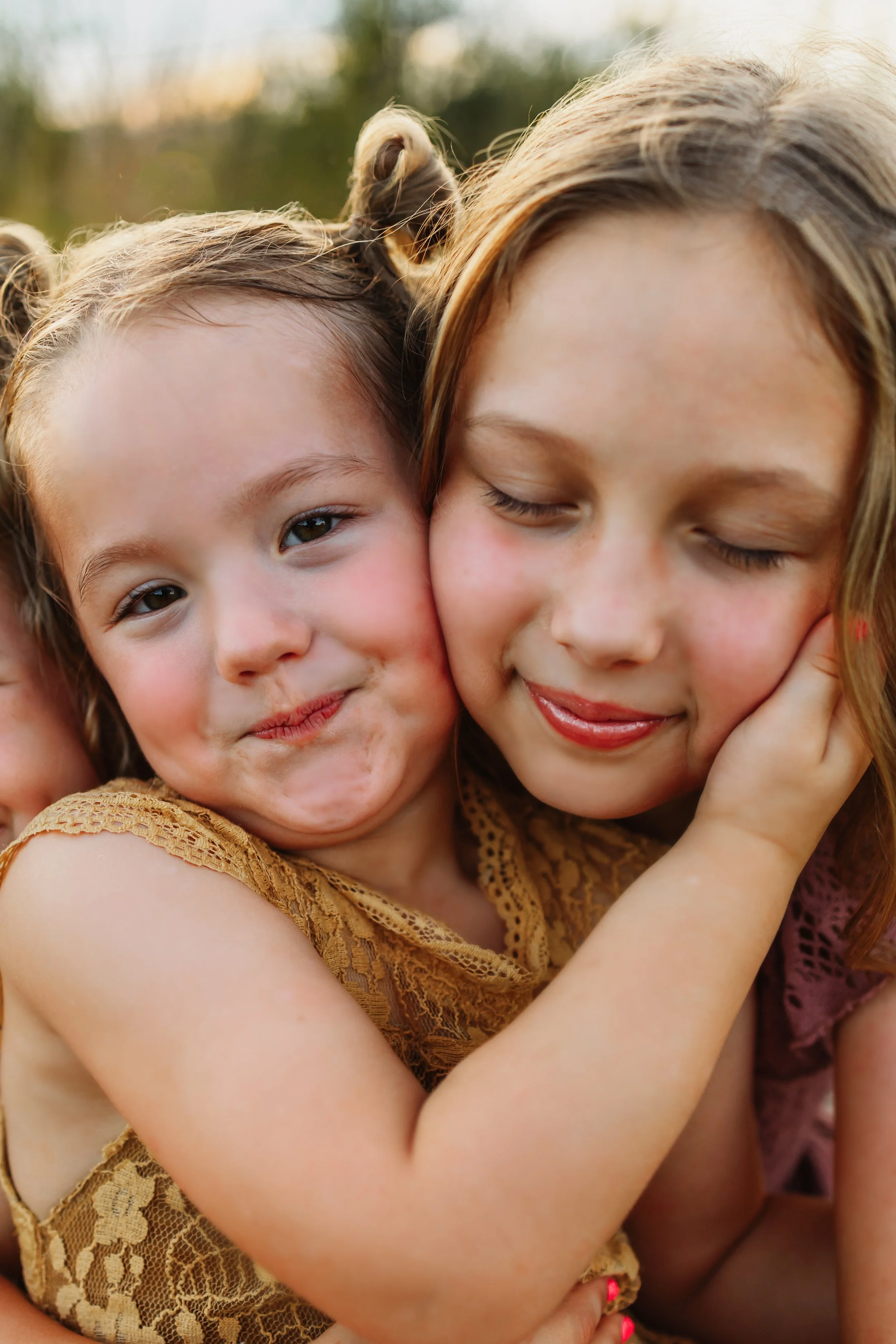 3 year old sister wrapping her arm around to place it on her sisters check, gently bringing her check to press against hers during a fall family pictures with Kristen Coberly Photography
