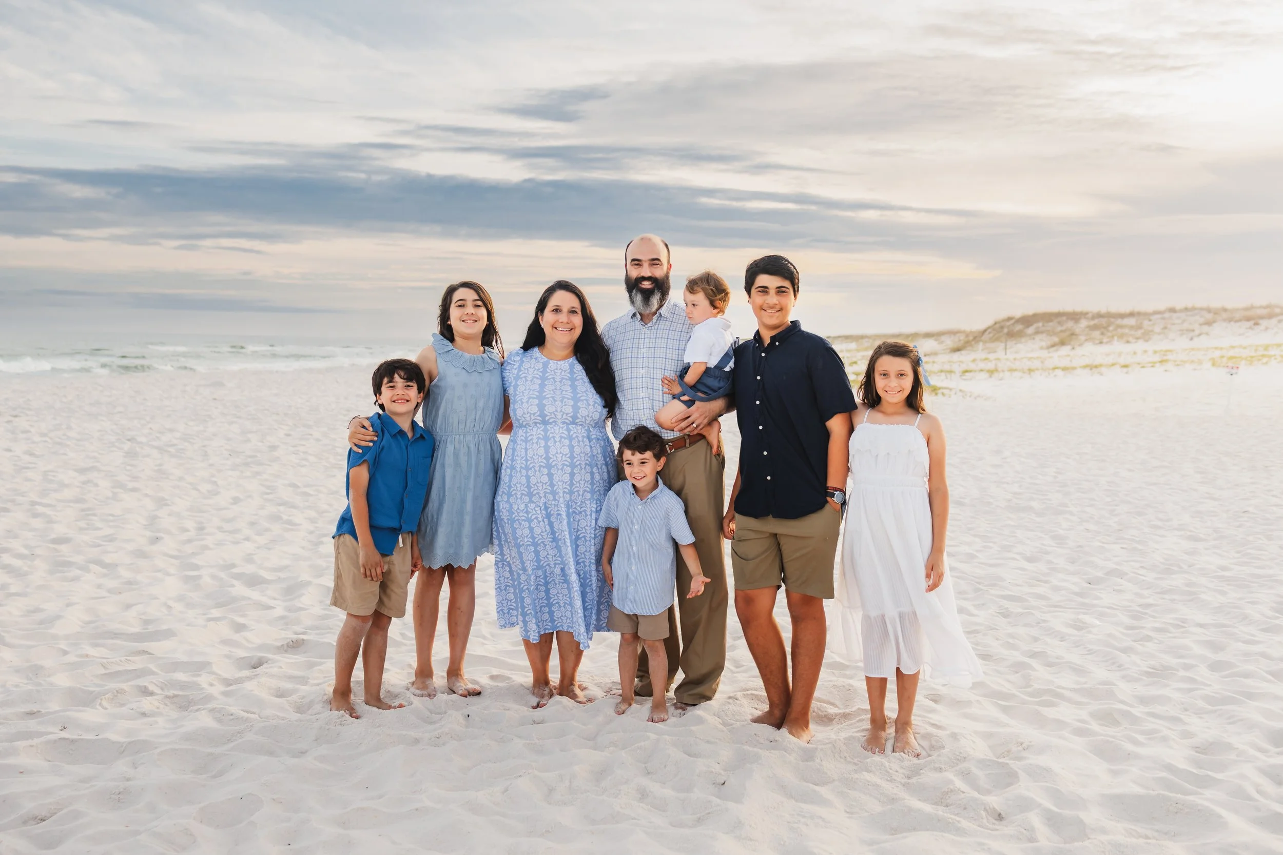 Family of 8 smiling for the camera while standing in the sand at Pensacola Beach during there photo session with Kristen Coberly Photography