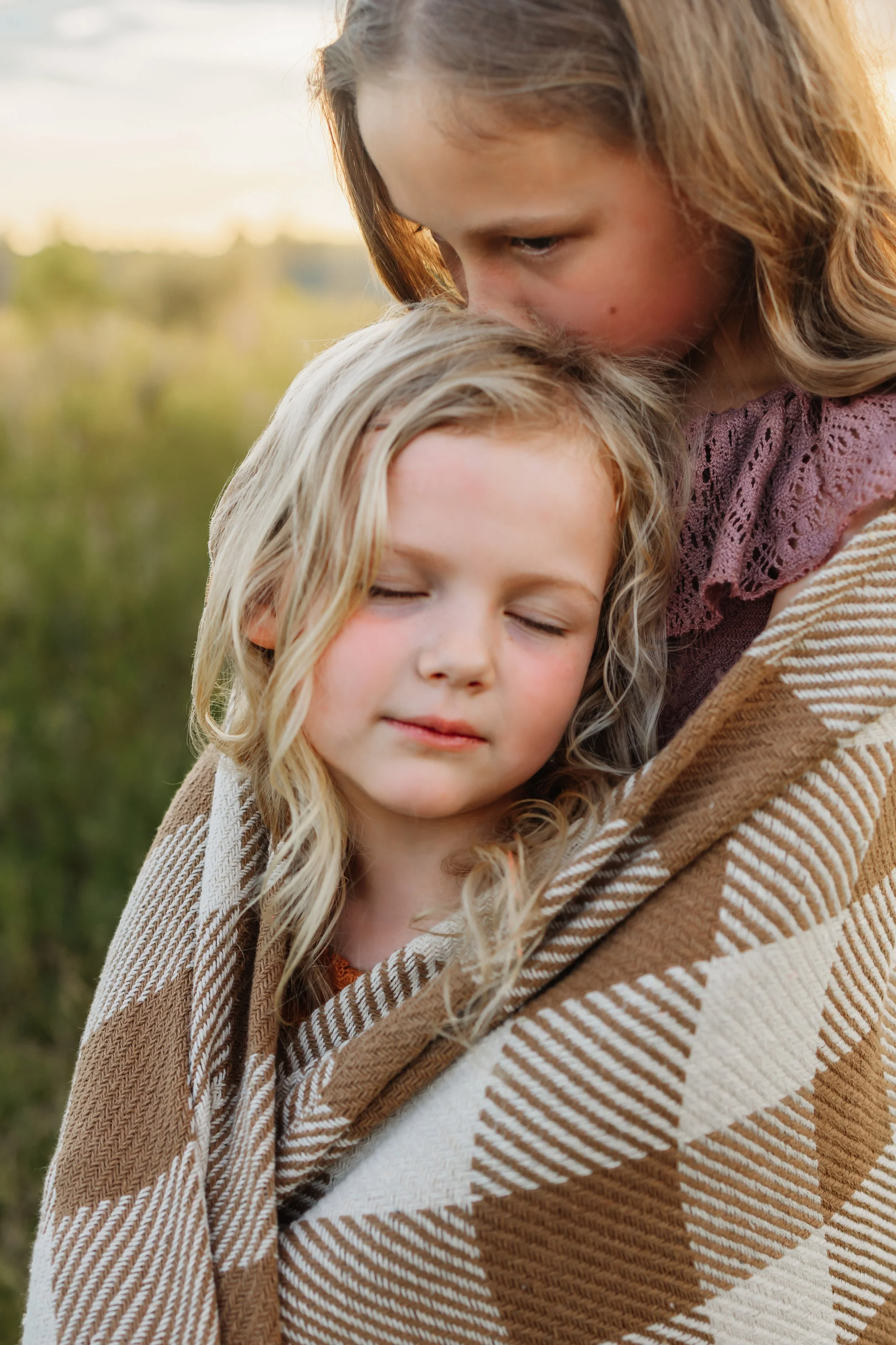 Older sister wrapping her arms around her younger sister kissing the top of her head while the younger sister closes her eyes enjoying the moment during a fall photoshoot with Kristen Coberly Photography