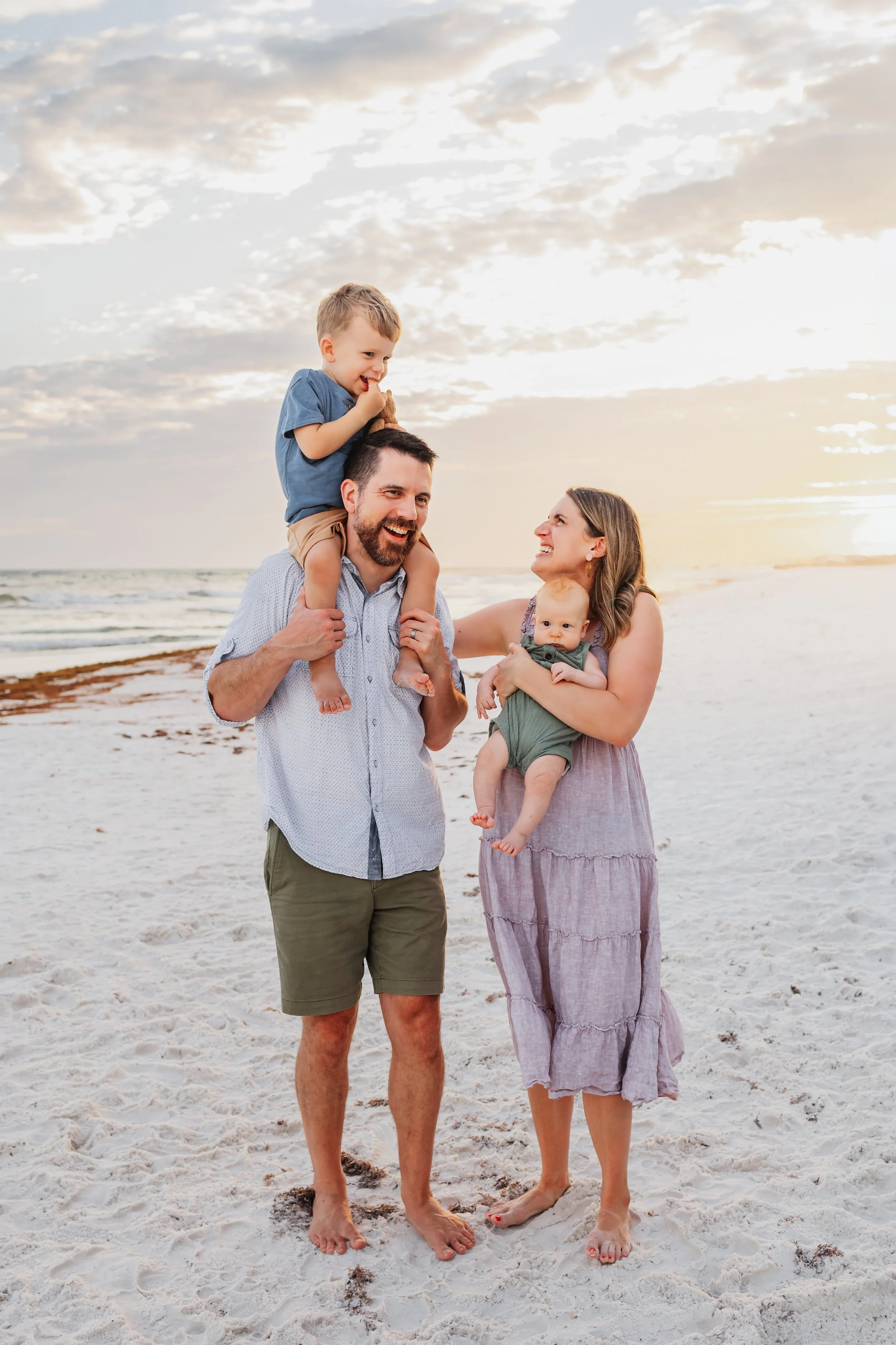 Family of four (with the toddler on dad's shoulders) tickling each other while posing for a photo session on Pensacola Beach with Kristen Coberly Photography