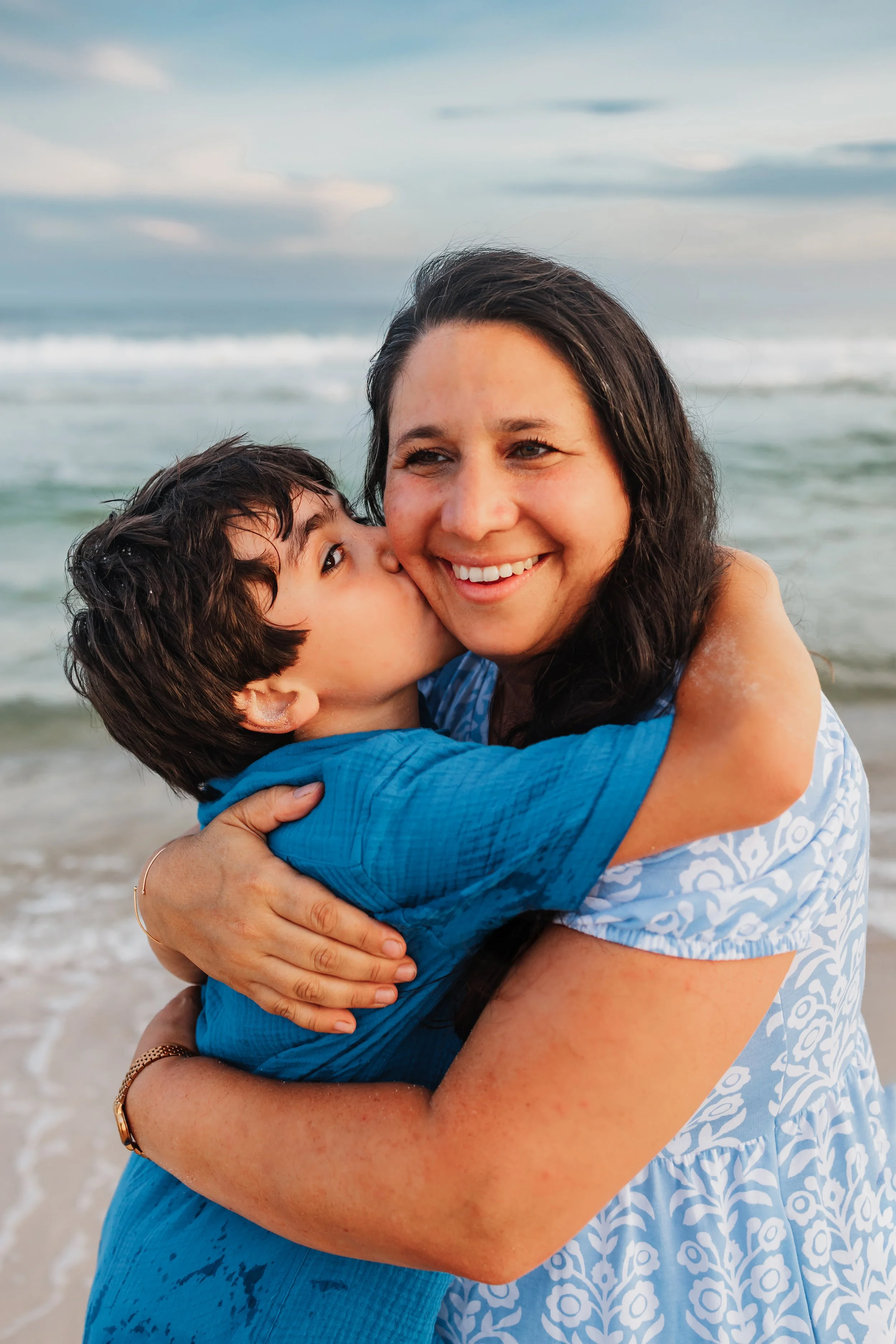 8 year old son giving mom a kiss on the cheek at the water's edge at Pensacola Beach during the family's photo session with Kristen Coberly Photography.
