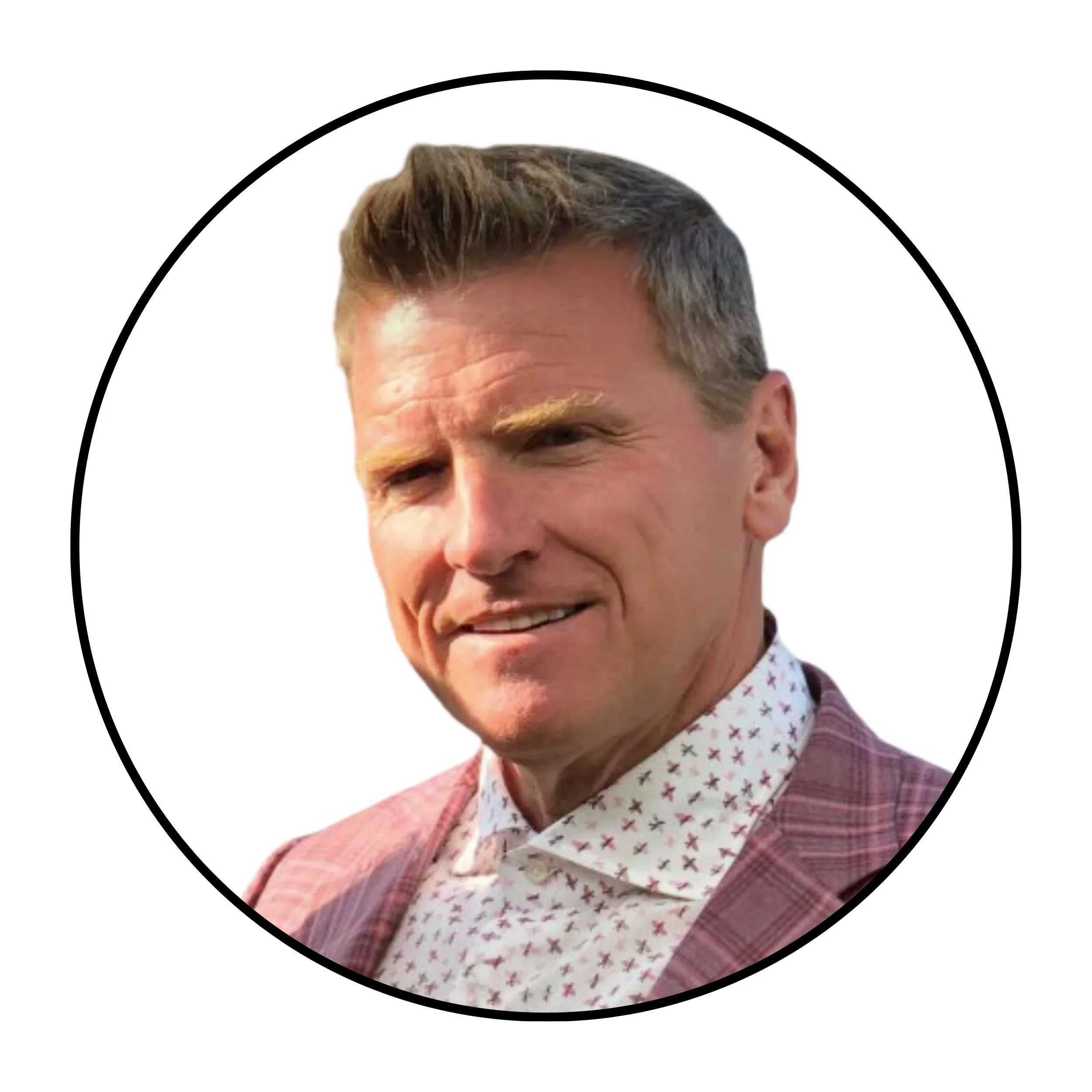 Close-up of a man with styled hair, smiling, dressed in a patterned shirt and a pink blazer, against a plain white background.