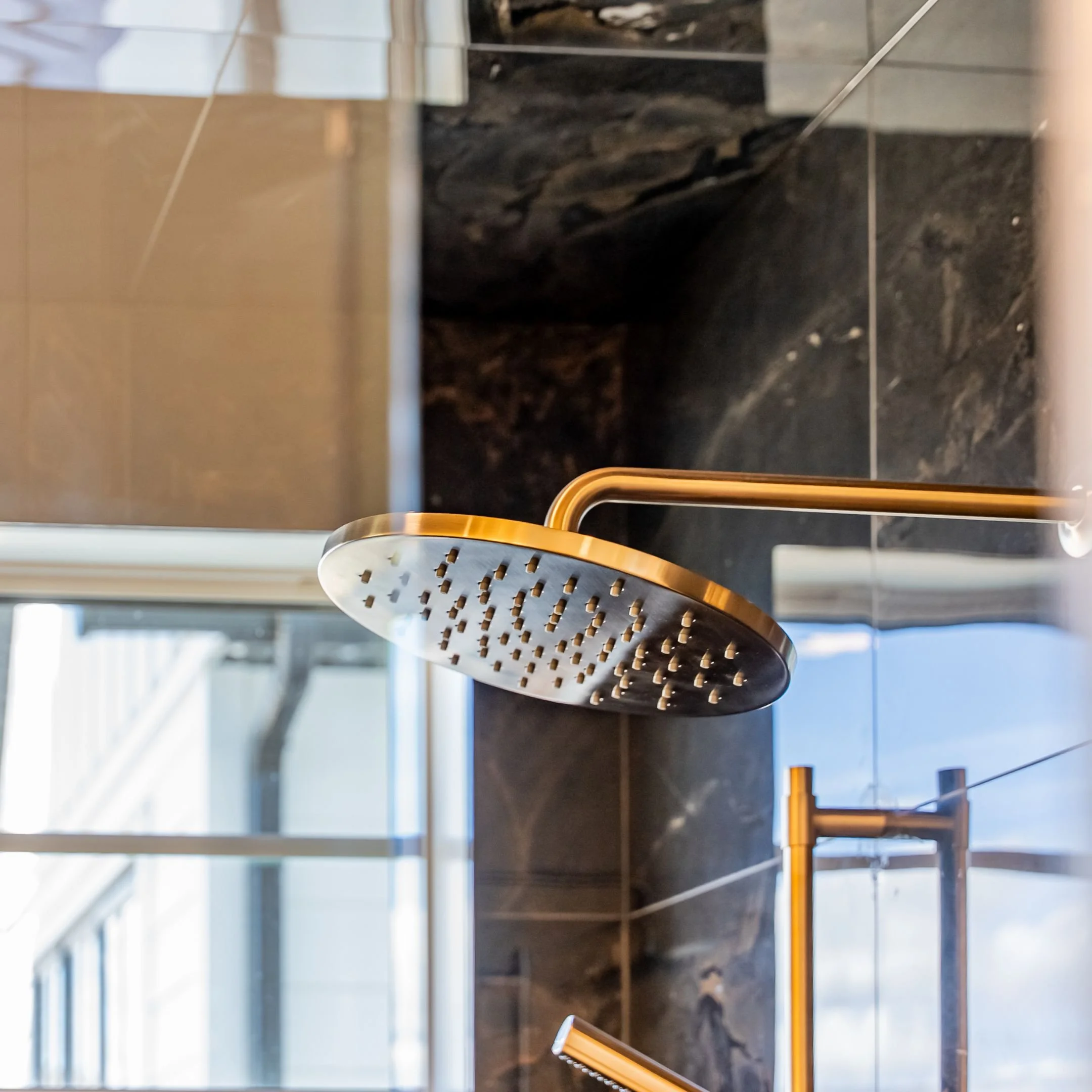 Close-up view of a black and dark gray marble wall with a metal showerhead, and part of a yellow towel rack with a wooden handle, in a modern bathroom.