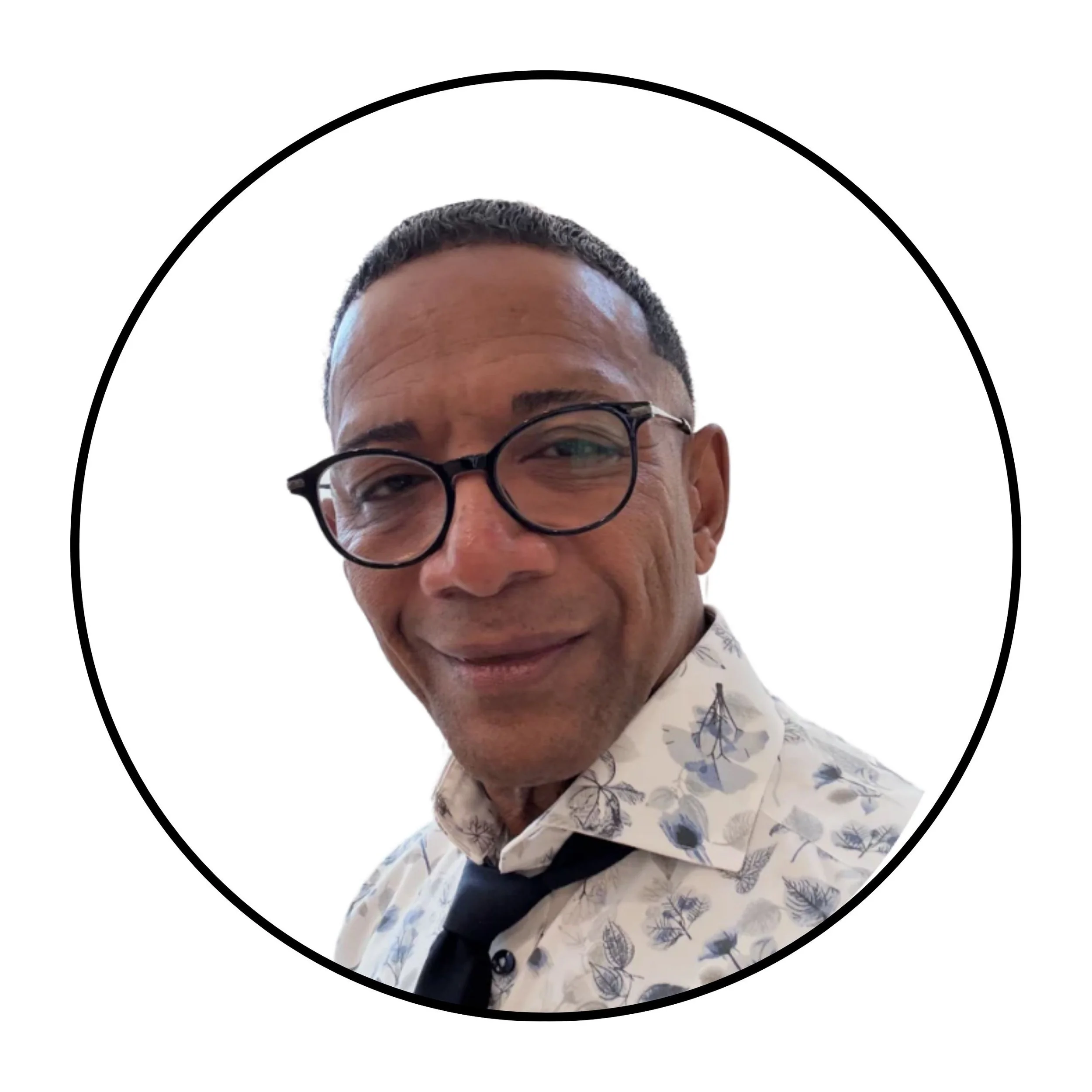 A person with short gray hair and glasses smiling, wearing a white shirt with a gray leaf pattern, against a white background.