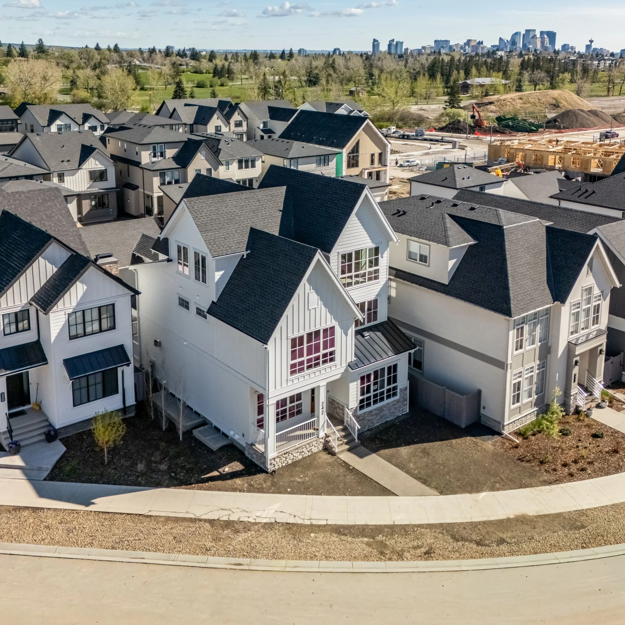 View of a suburban residential area with new construction homes and a city skyline in the distance under a partly cloudy sky.