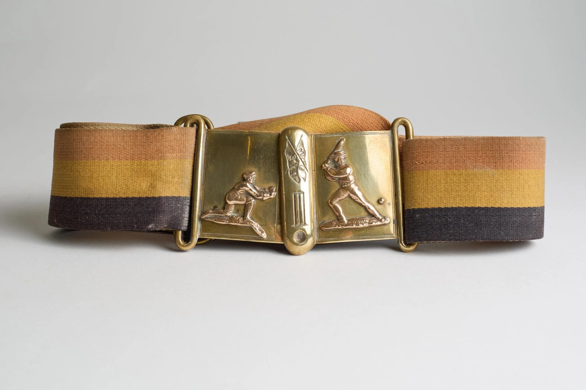 Lot 396
'United All England XI'. Early and complete material belt in colour bands of I'Zingari with excellent two piece brass belt buckle with applied figures of a batsman about to strike the ball on one piece and a wicket-keeper ready to catch on t