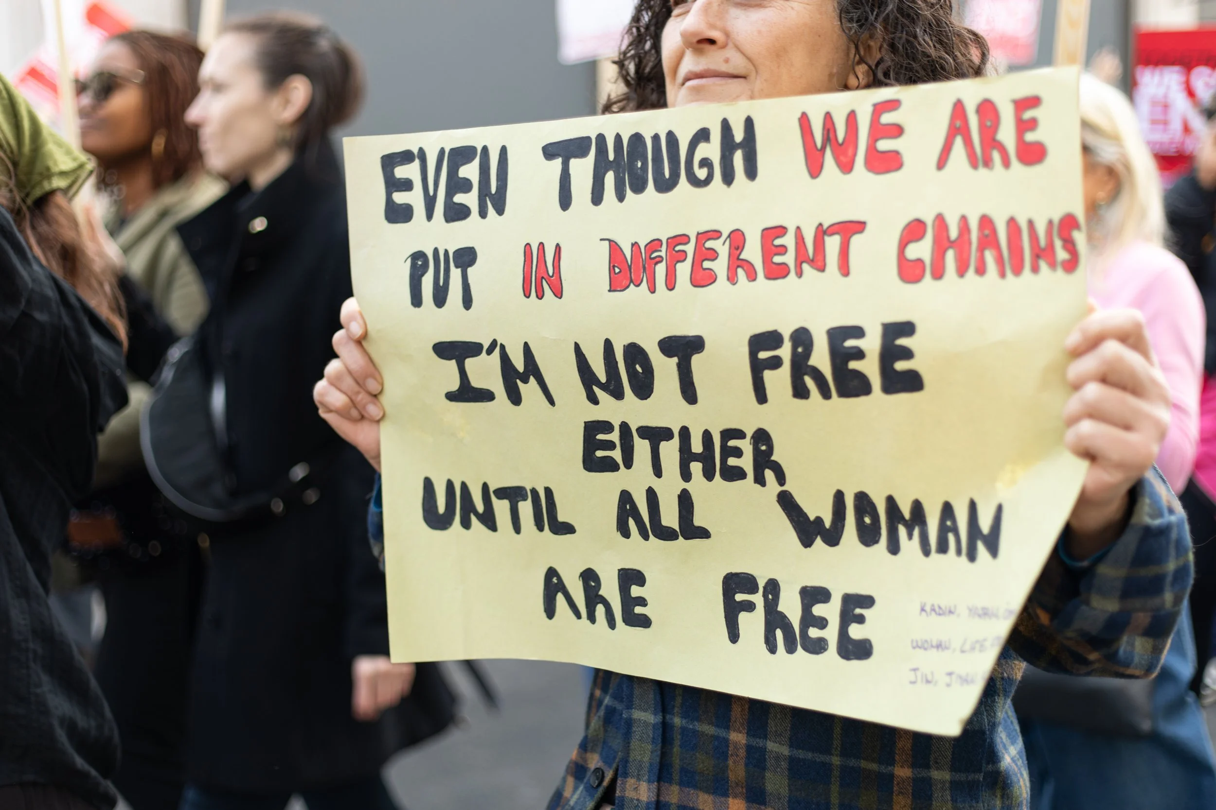 A woman at a protest holding a yellow sign with a message advocating for women's freedom, with other protestors in the background.