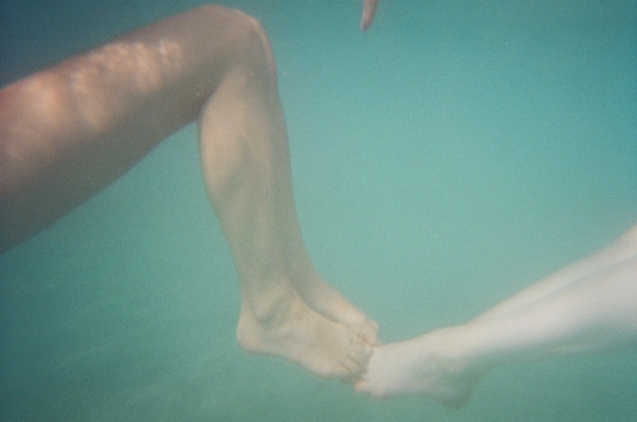 A person is underwater, kicking their legs and holding a white towel or cloth with their feet, against a blue-green background.