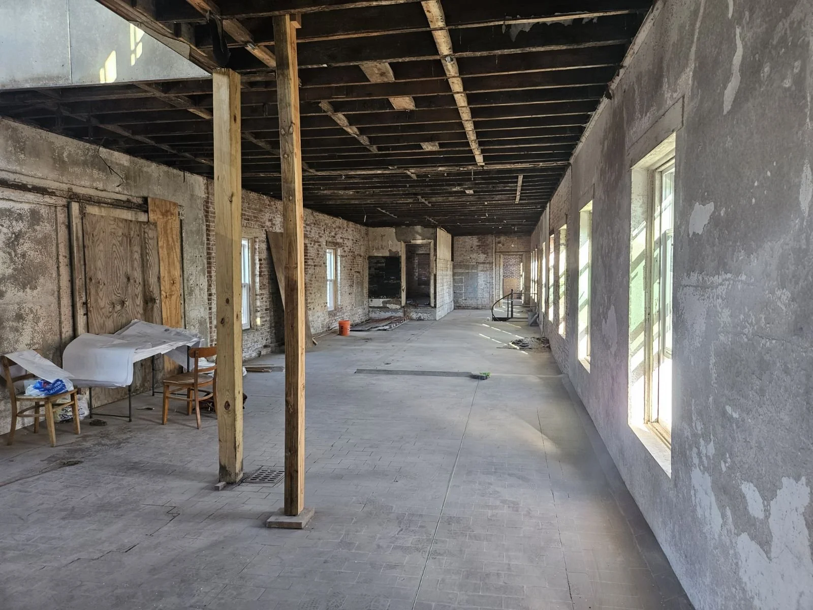 Long factory hallway with cement floors and wood beams and ceiling. Light streams through windows.