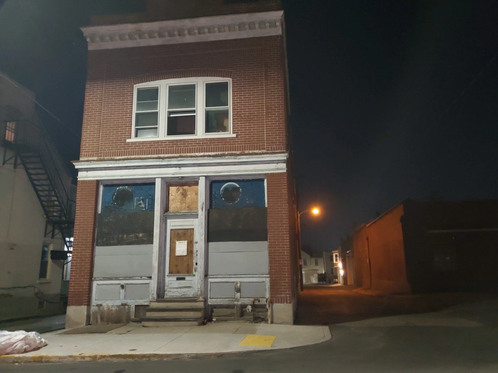 Two-story brick building with boarded windows and door under night sky