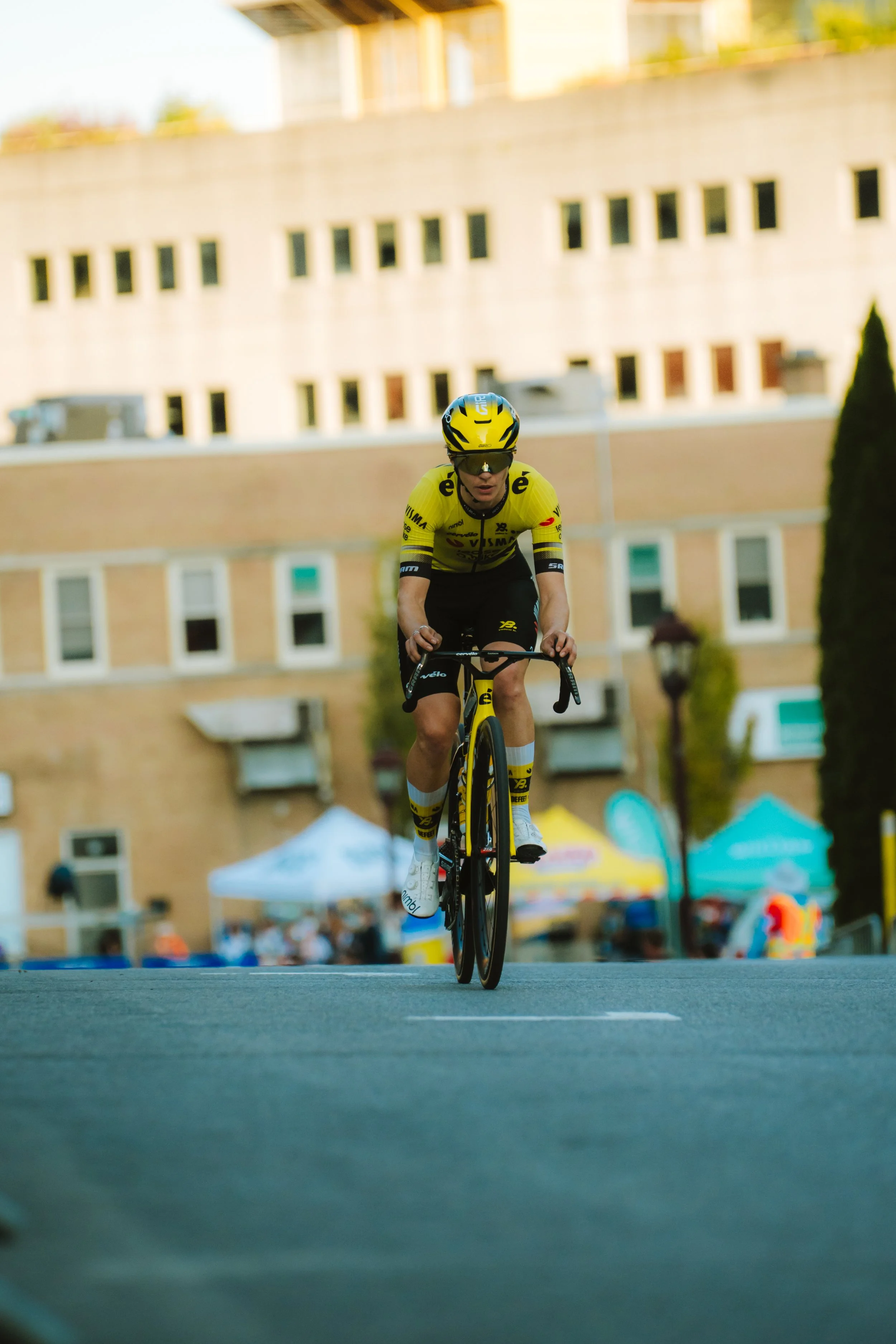 A cyclist in yellow attire riding a bike on a street during a race or event.