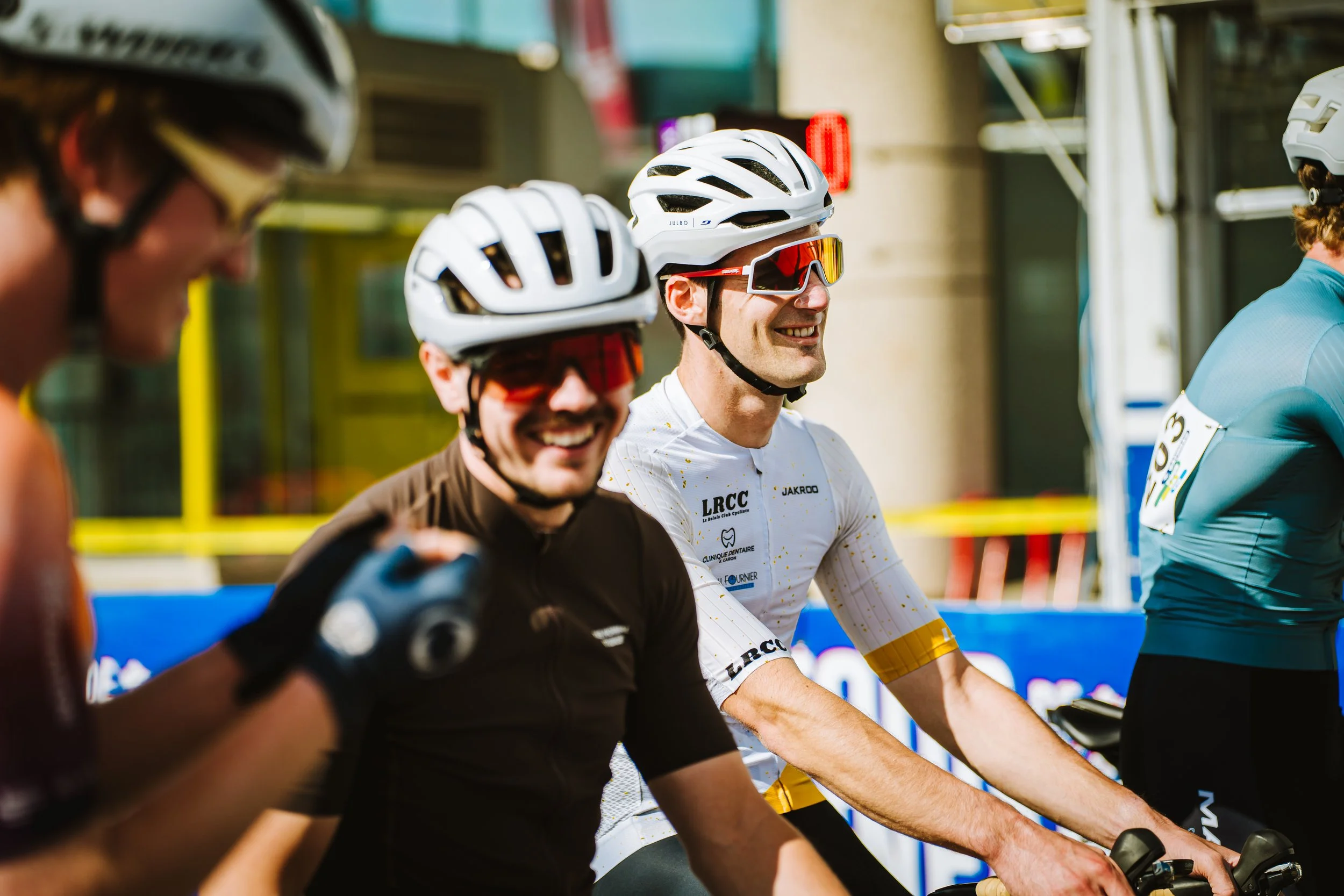 Four cyclists in helmets and sunglasses smiling, preparing for a race or event.