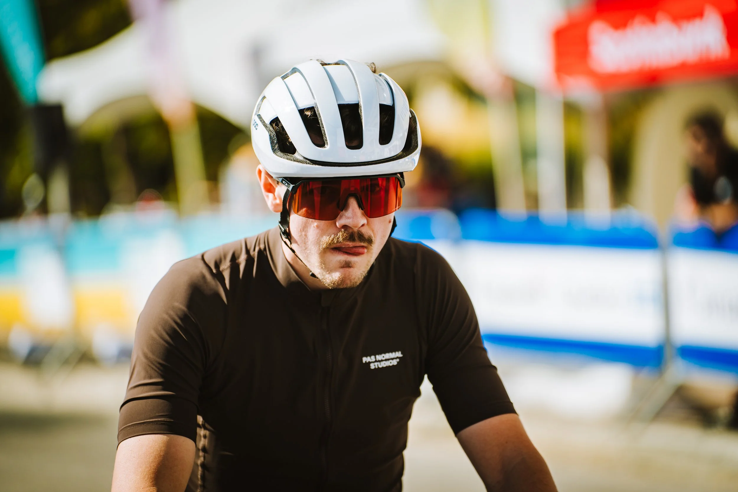 Male cyclist wearing a white helmet, red sunglasses, and a black cycling jersey at an outdoor event.