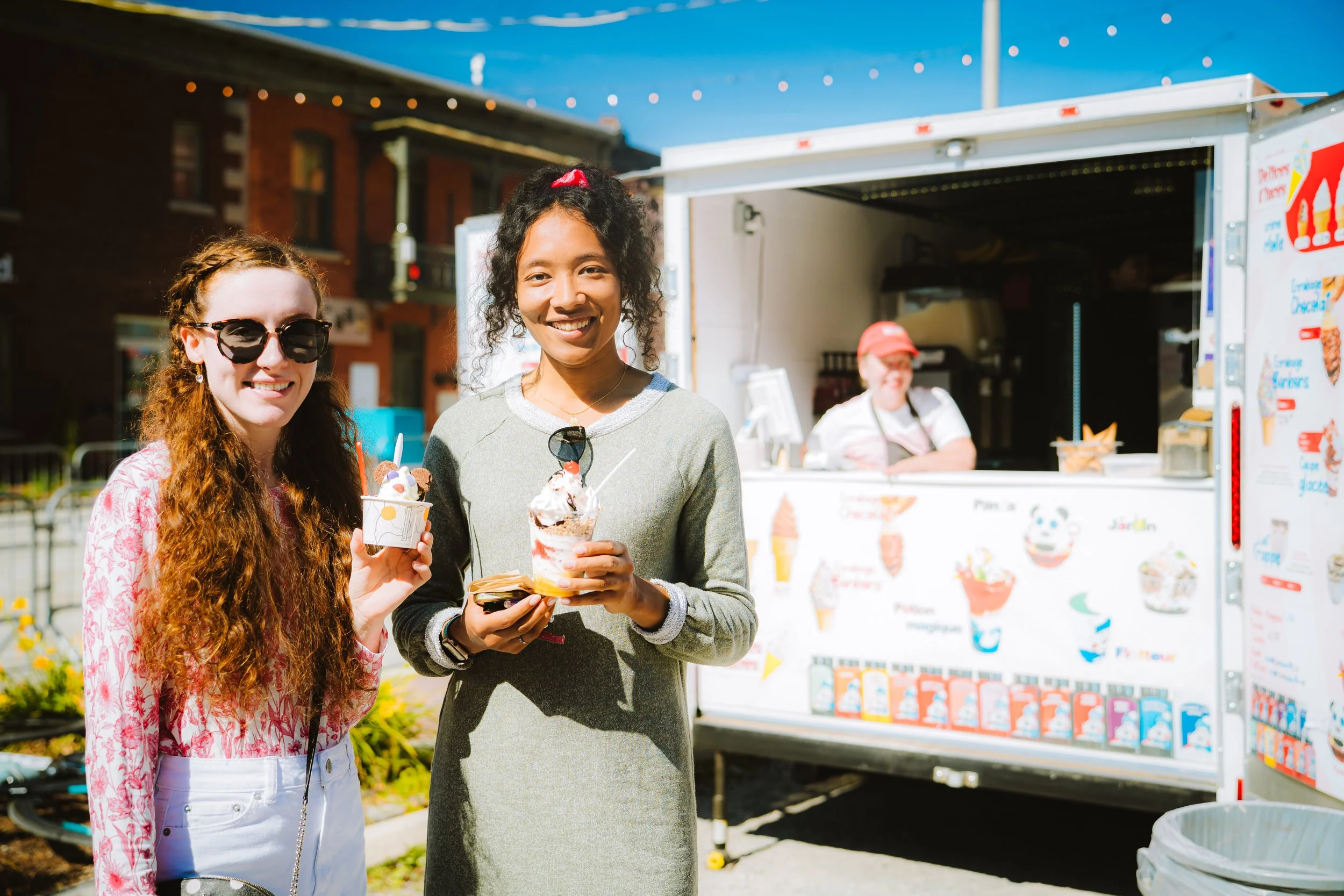 Two women enjoying ice cream in front of a food truck on a sunny day.