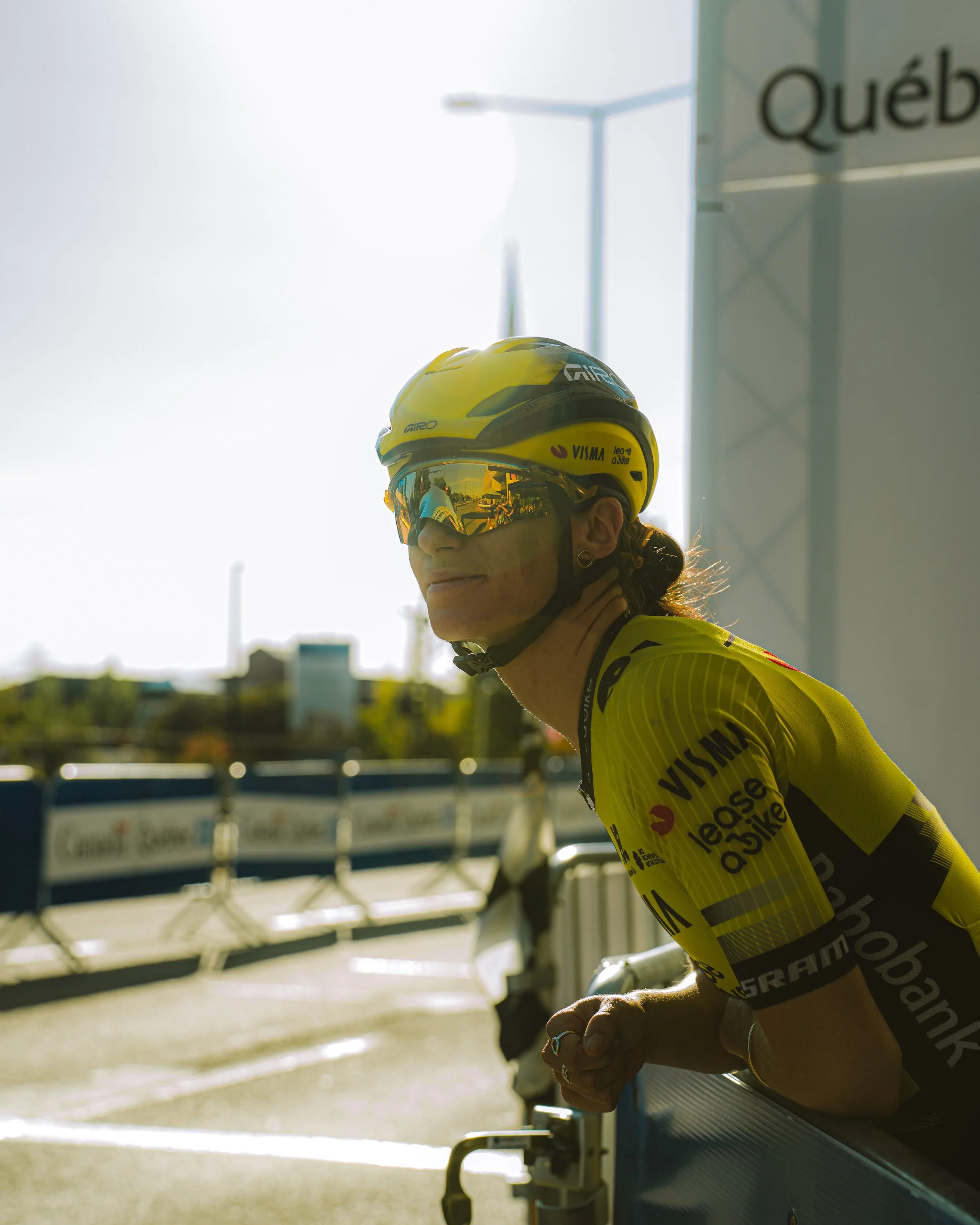 A female cyclist wearing a yellow helmet and sunglasses, leaning on a barrier at a cycling event.
