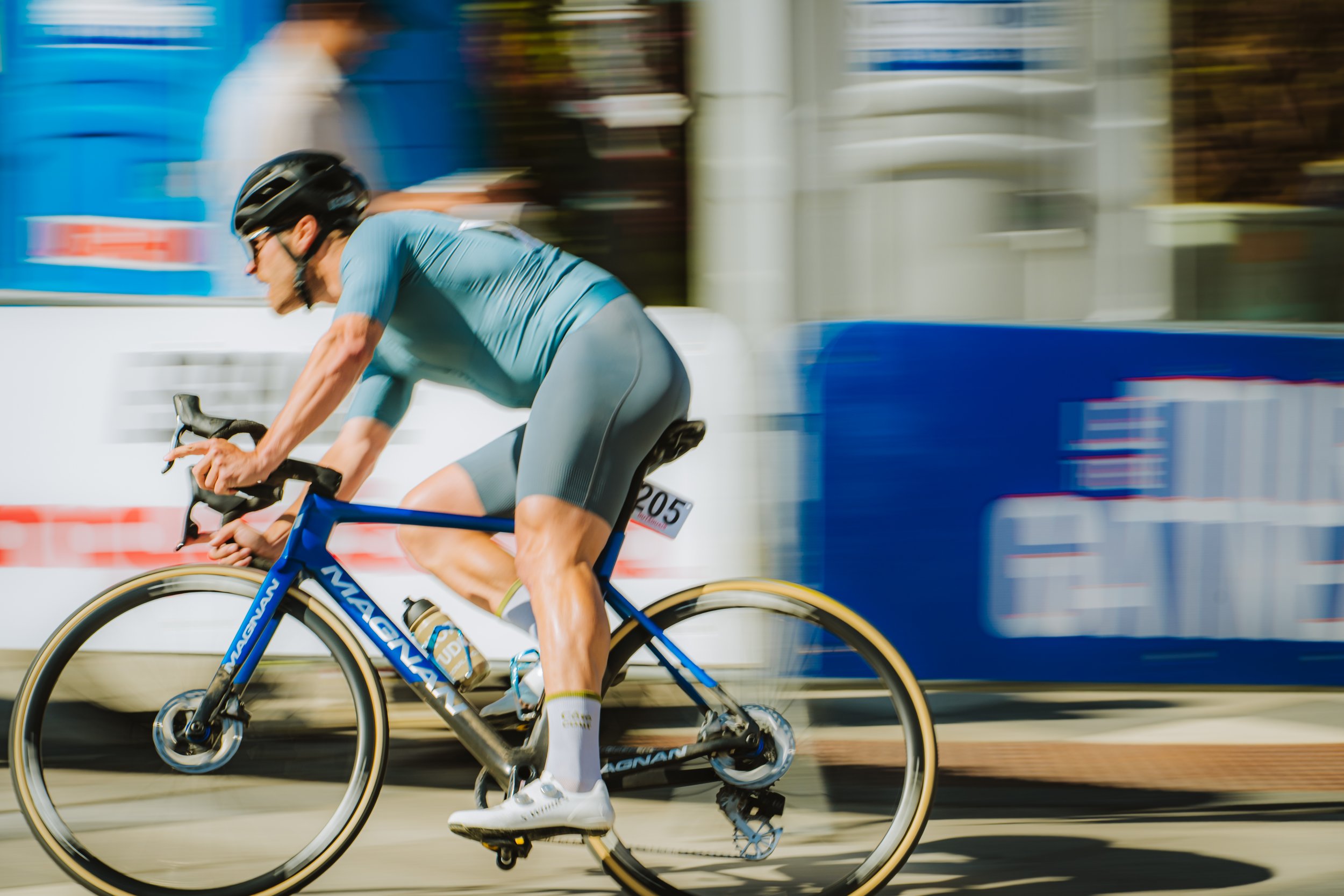 Multicolor photograph of a male cyclist in motion riding a blue and black bicycle on a street.