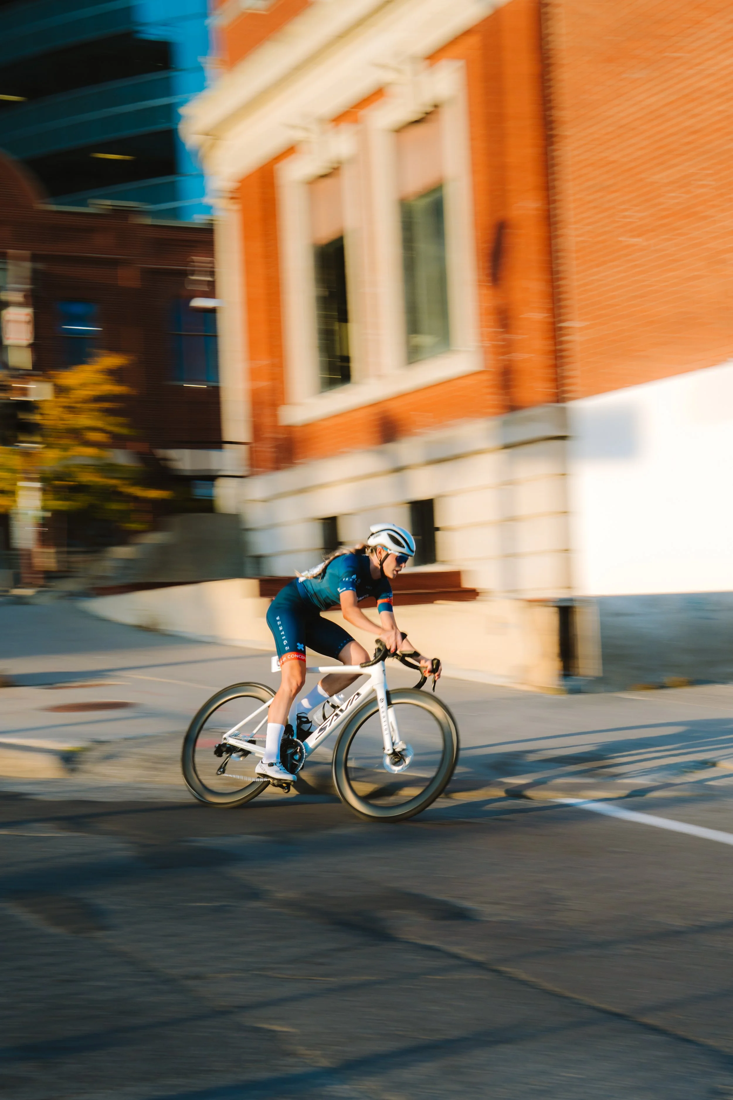 A person in cycling gear riding a white bicycle on a city street with blurred background buildings.