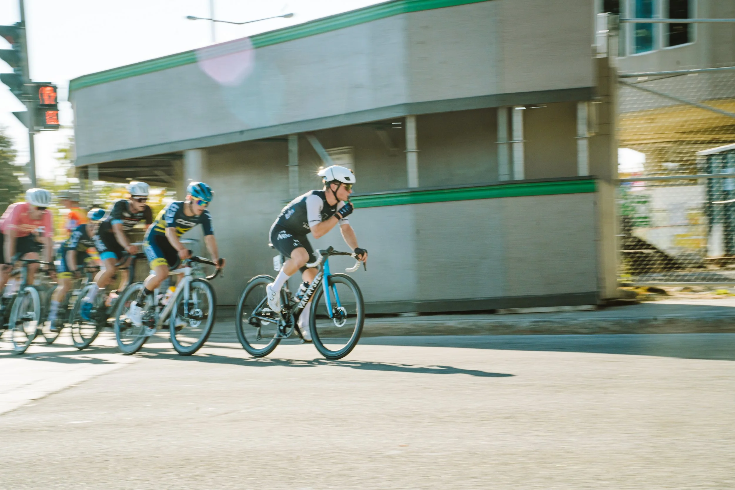 Cyclists participating in a race, riding on a city road under a bridge, wearing helmets and sports gear.