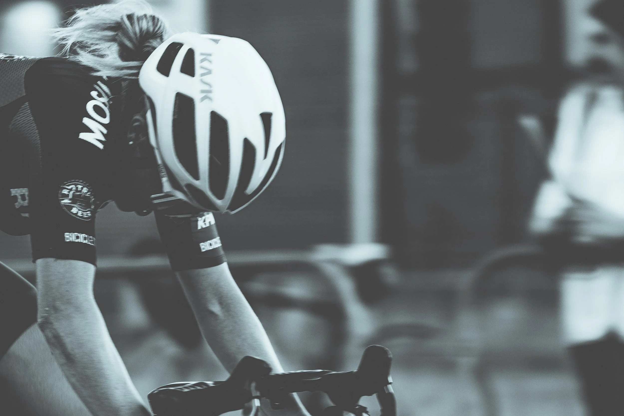 A cyclist wearing a helmet and sports gear, leaning forward on their bicycle, preparing for a ride indoors.