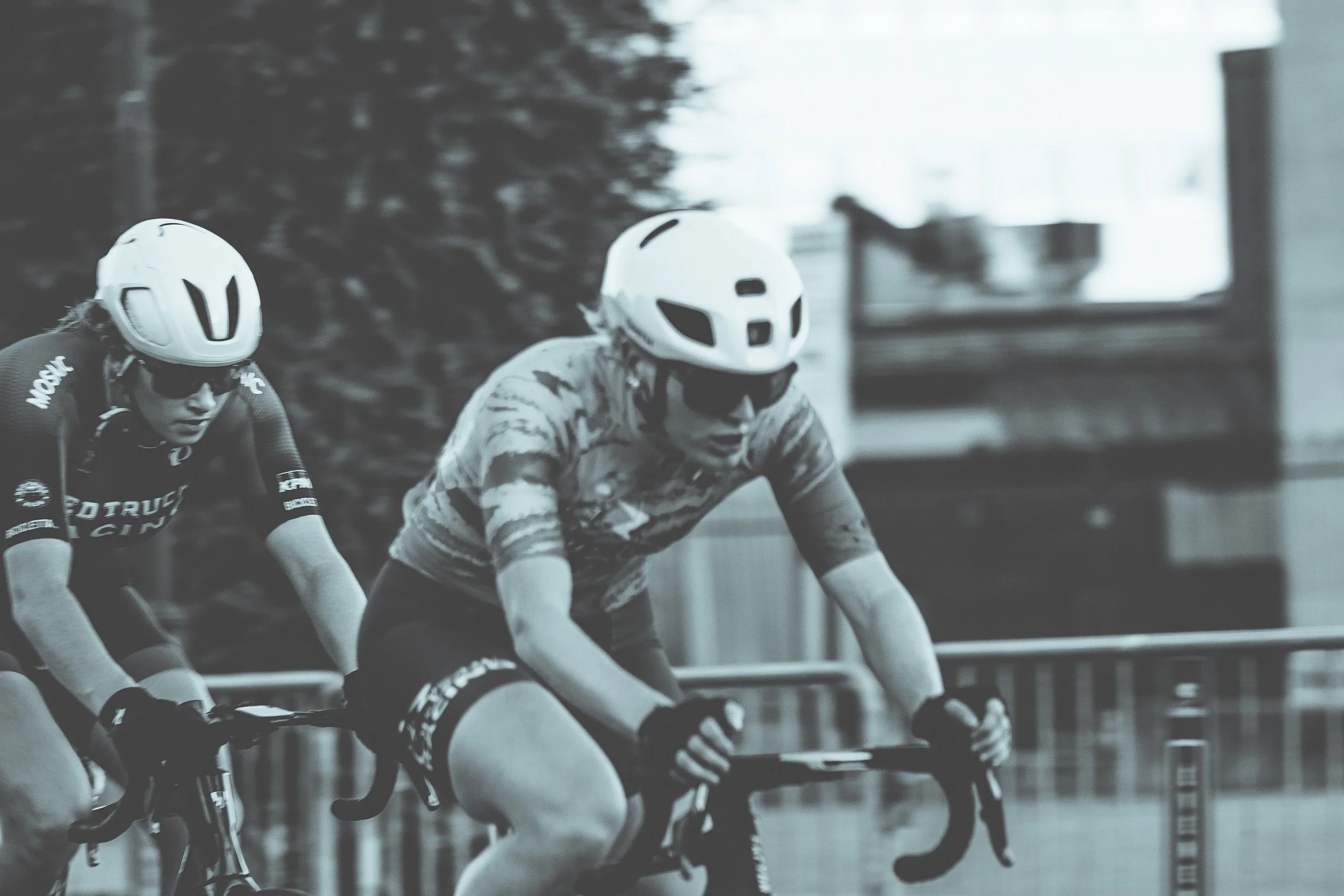 Two cyclists in helmets and cycling gear riding indoors on a track.