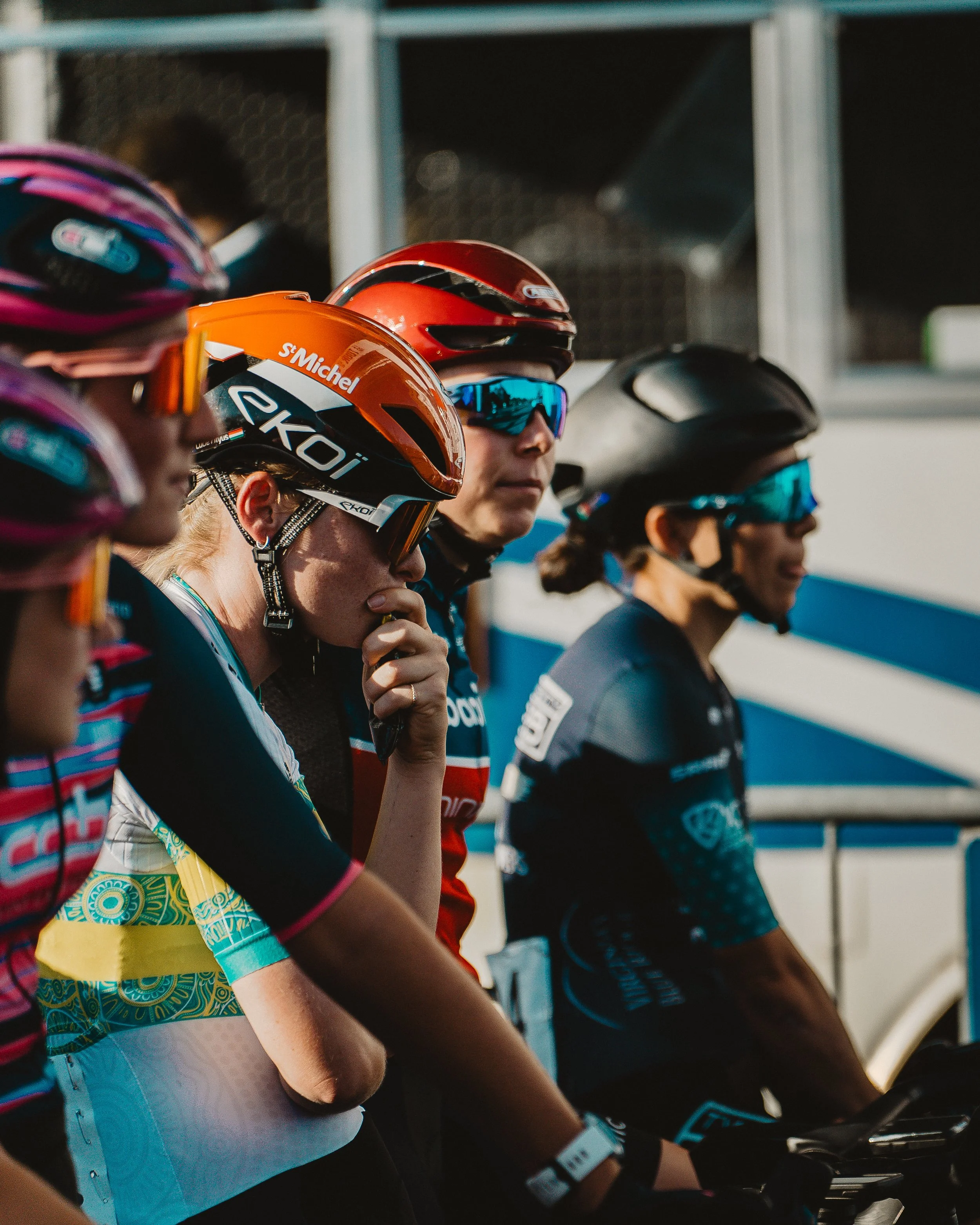 Group of female cyclists wearing helmets and sunglasses, ready for a race or ride.
