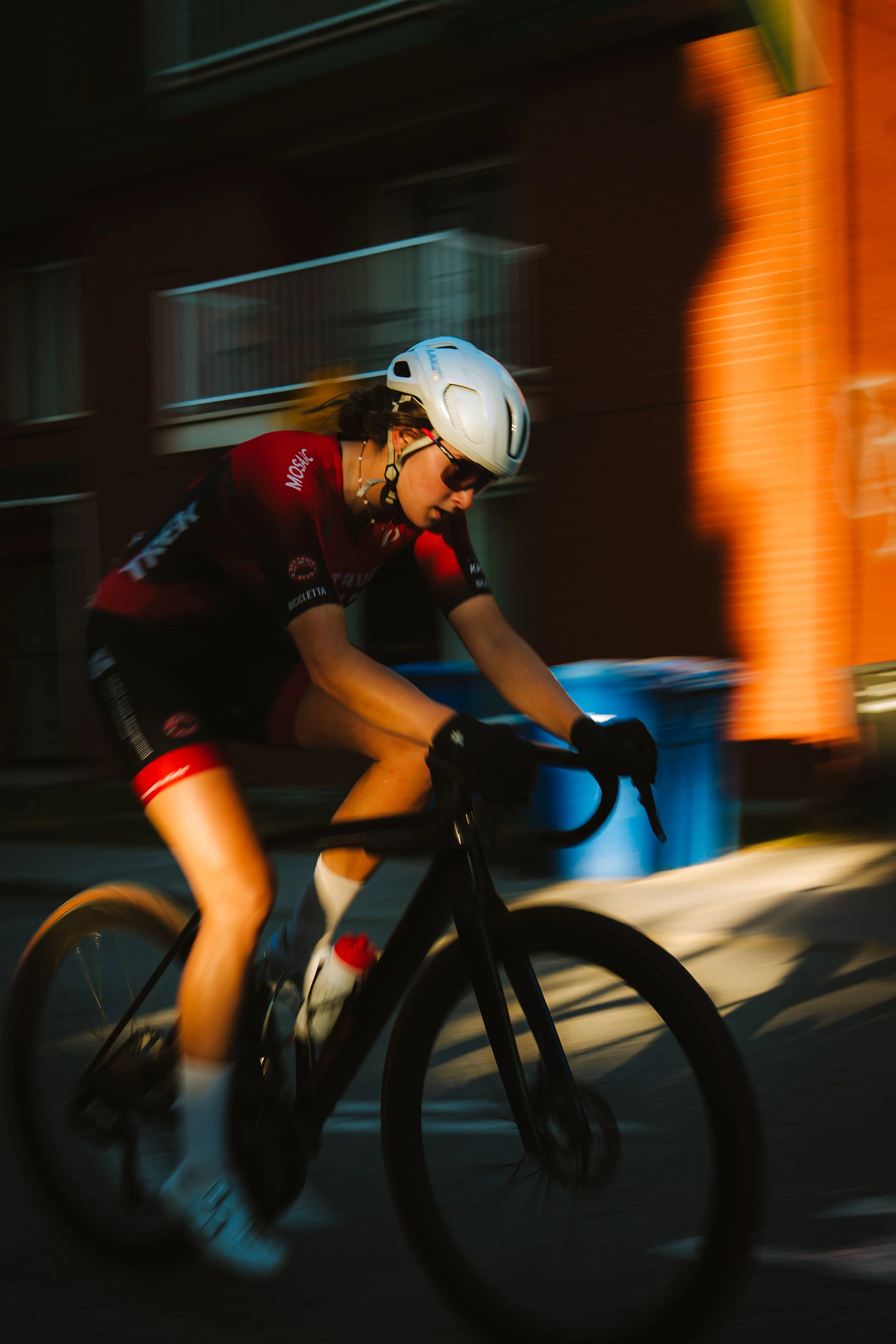 Cyclist riding a black bike during sunset, with motion blur and urban background.