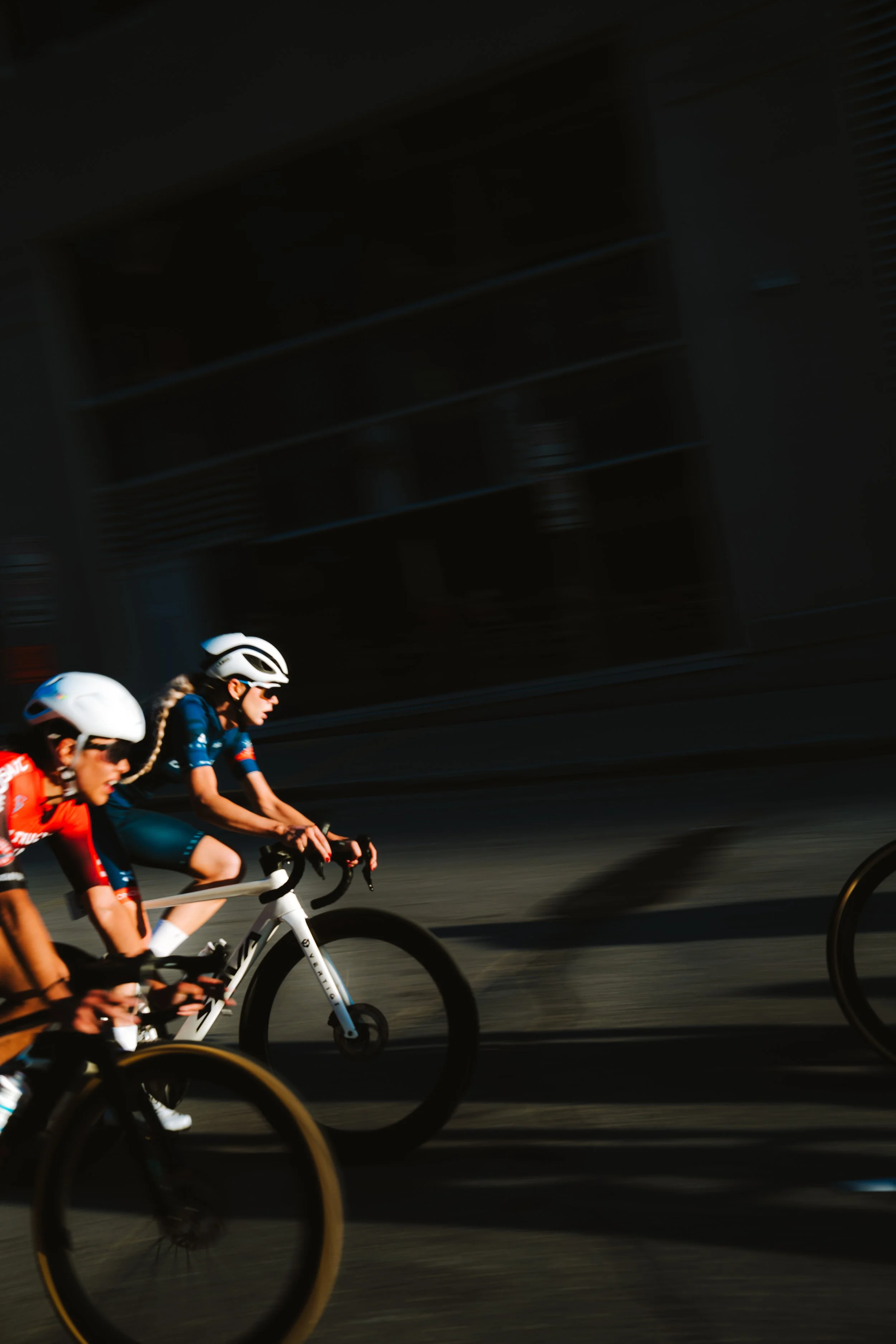 Three women riding bikes outside on a sunny day, wearing helmets and athletic clothing.
