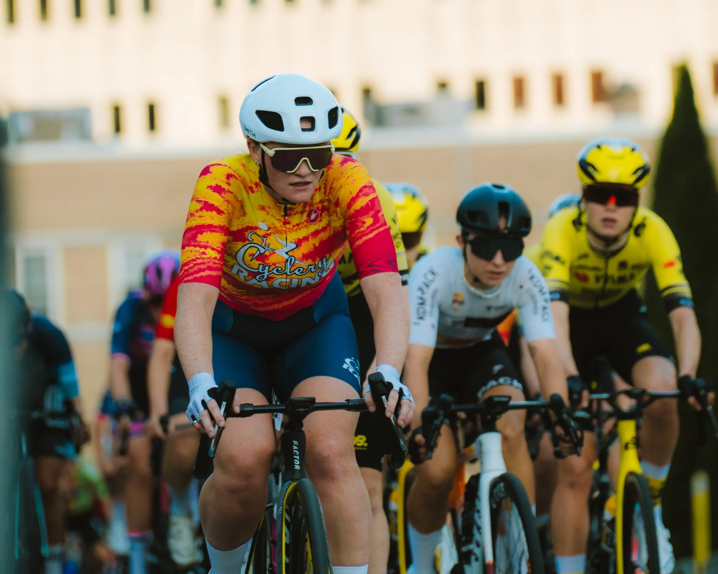 Cyclists participating in a race, wearing helmets and colorful jerseys, riding mountain bikes on a city street.