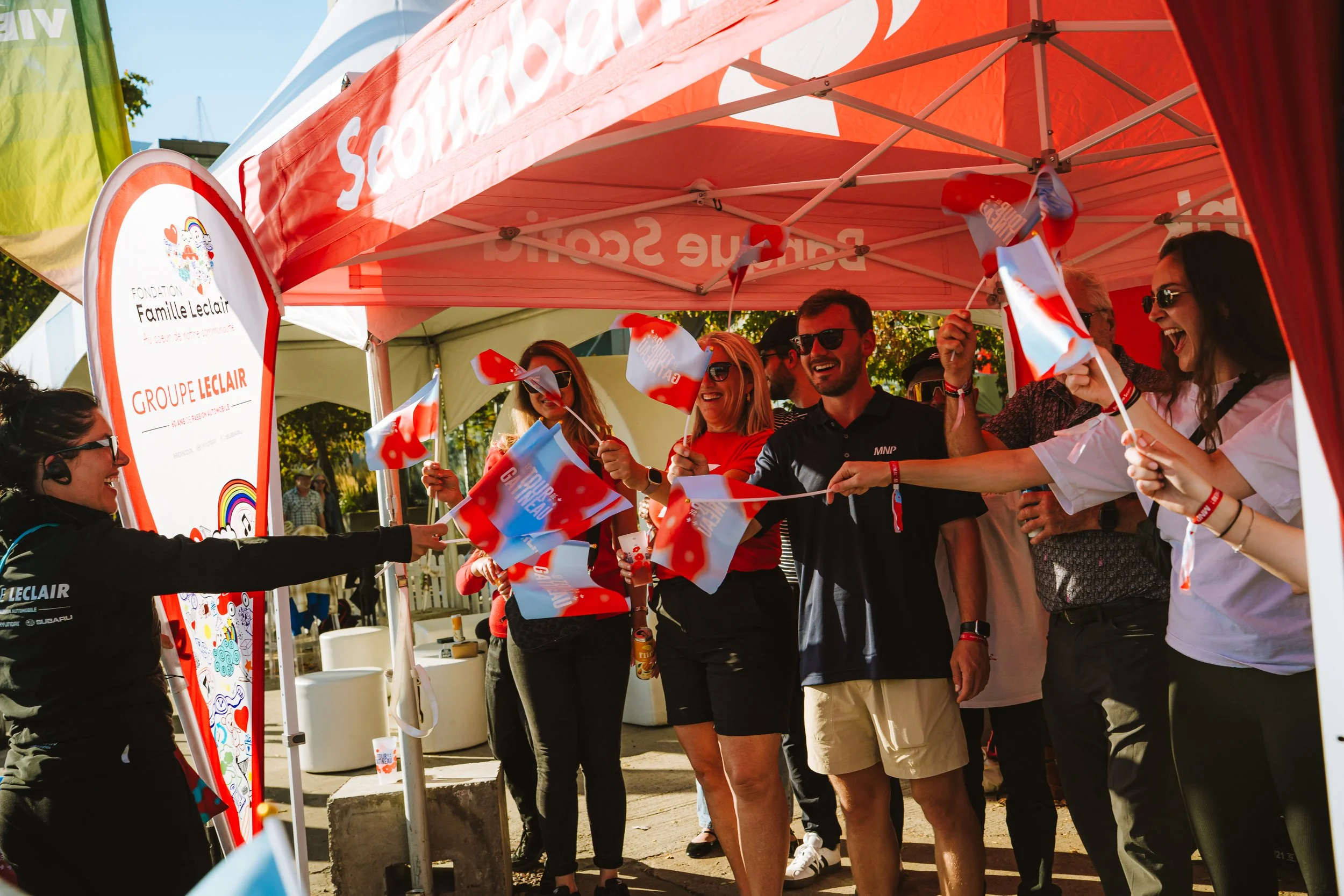 Group of people celebrating under a red canopy, waving small flags, smiling and having fun.