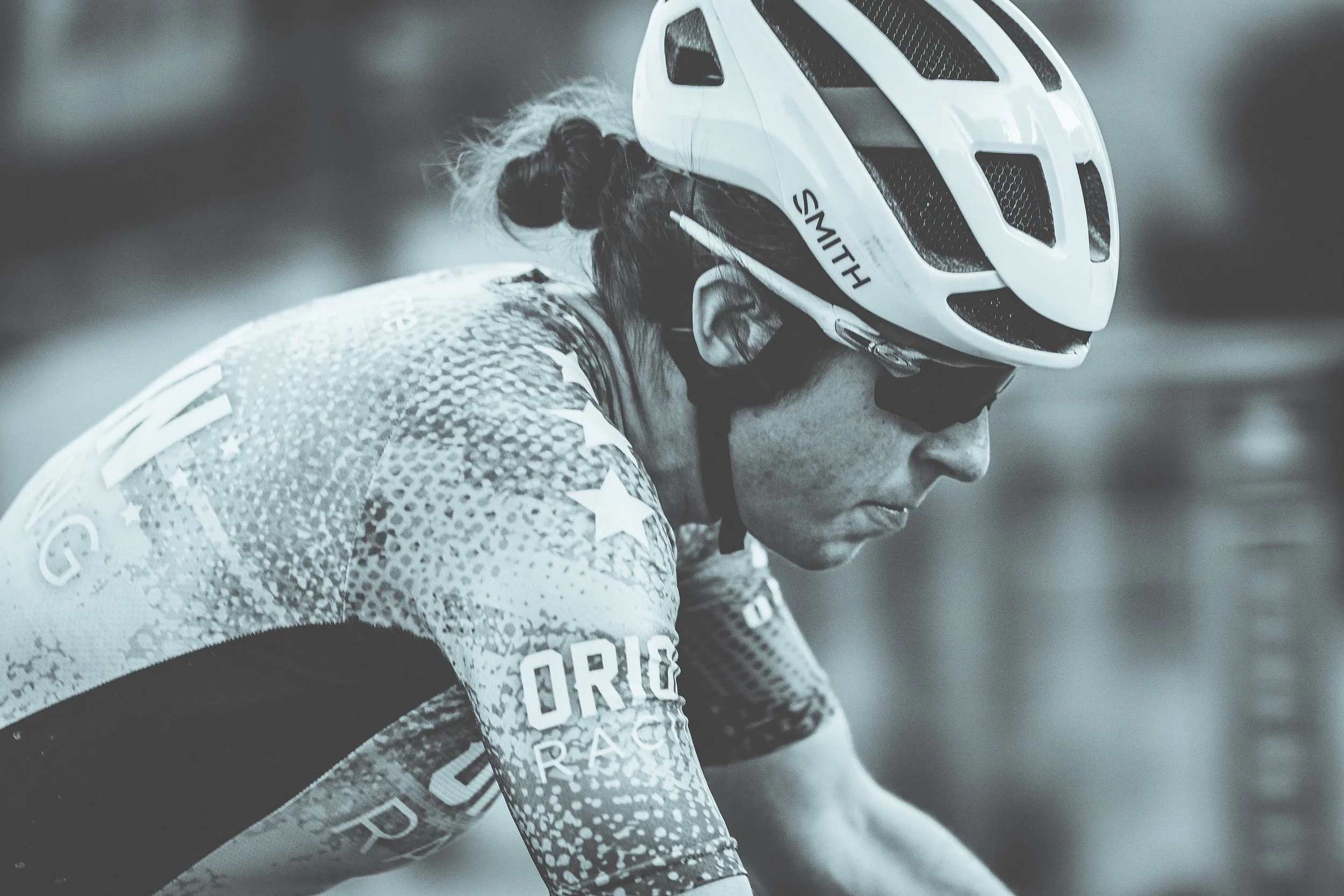 A person wearing a helmet and sunglasses, dressed in a racing jersey, looking down and focused during a race or training session.