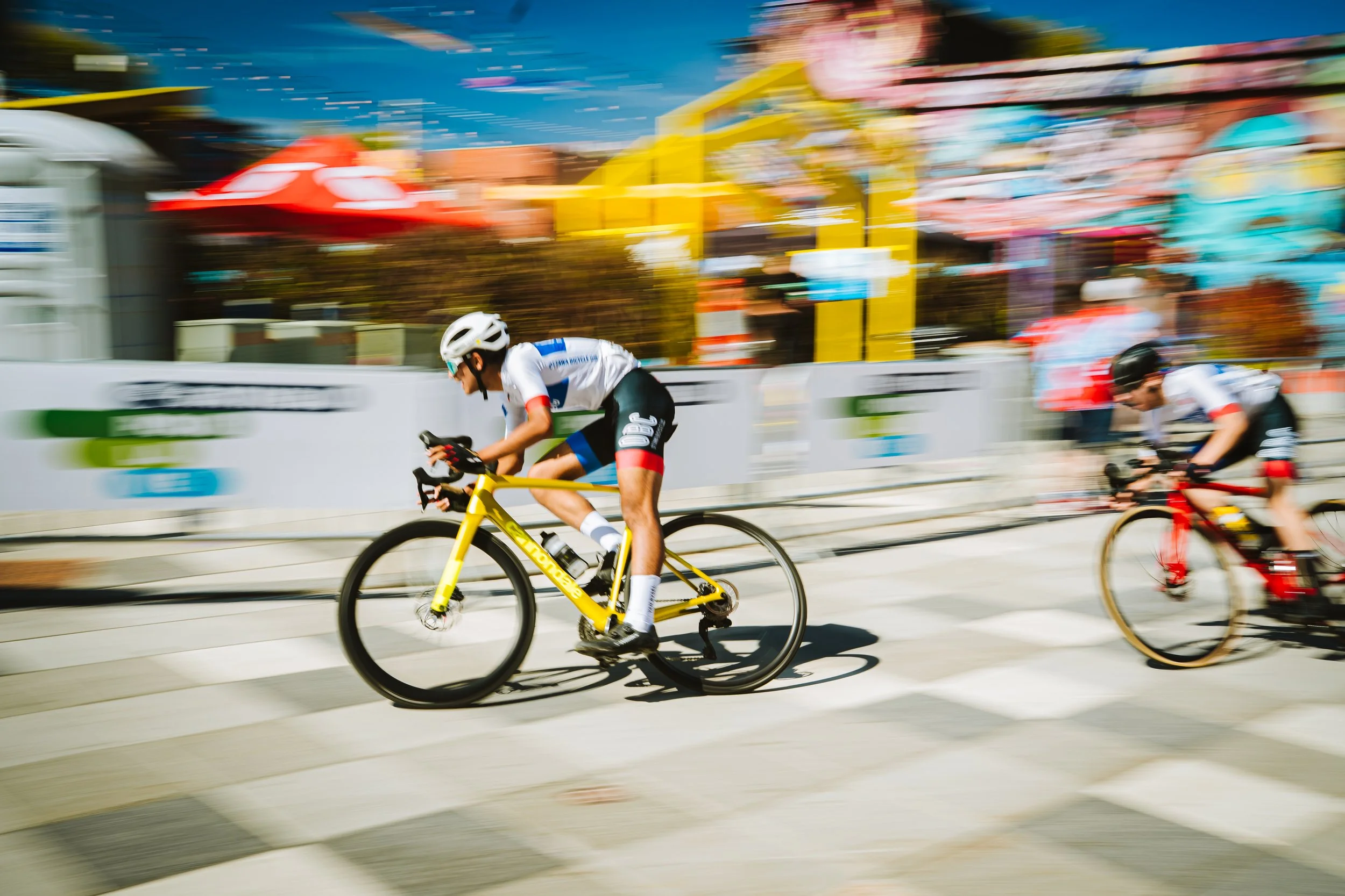 Two cyclists riding bikes in a race with colorful background and a blur effect.