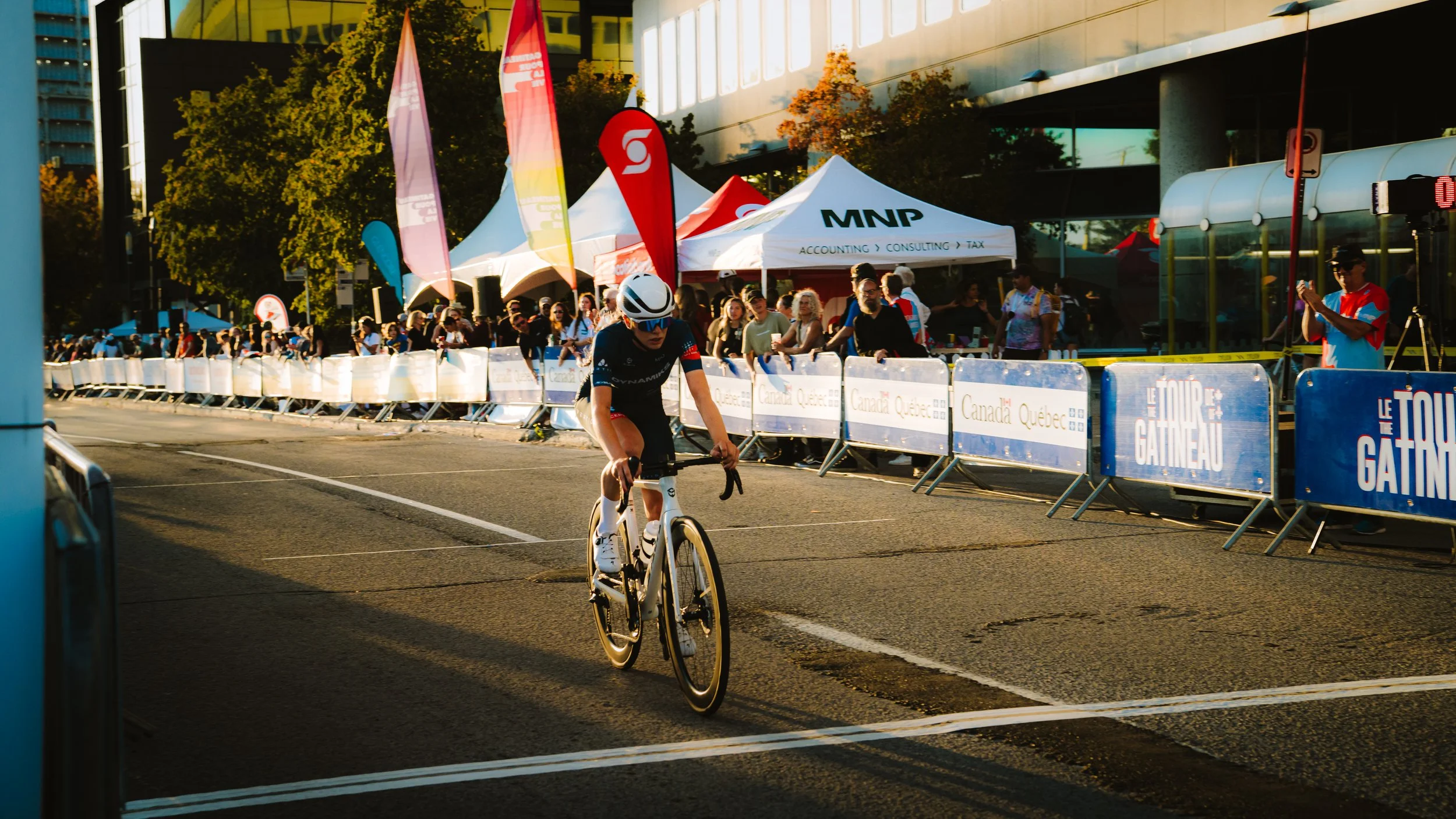 Cyclist crossing the finish line during a race with spectators and banners lined along the street.