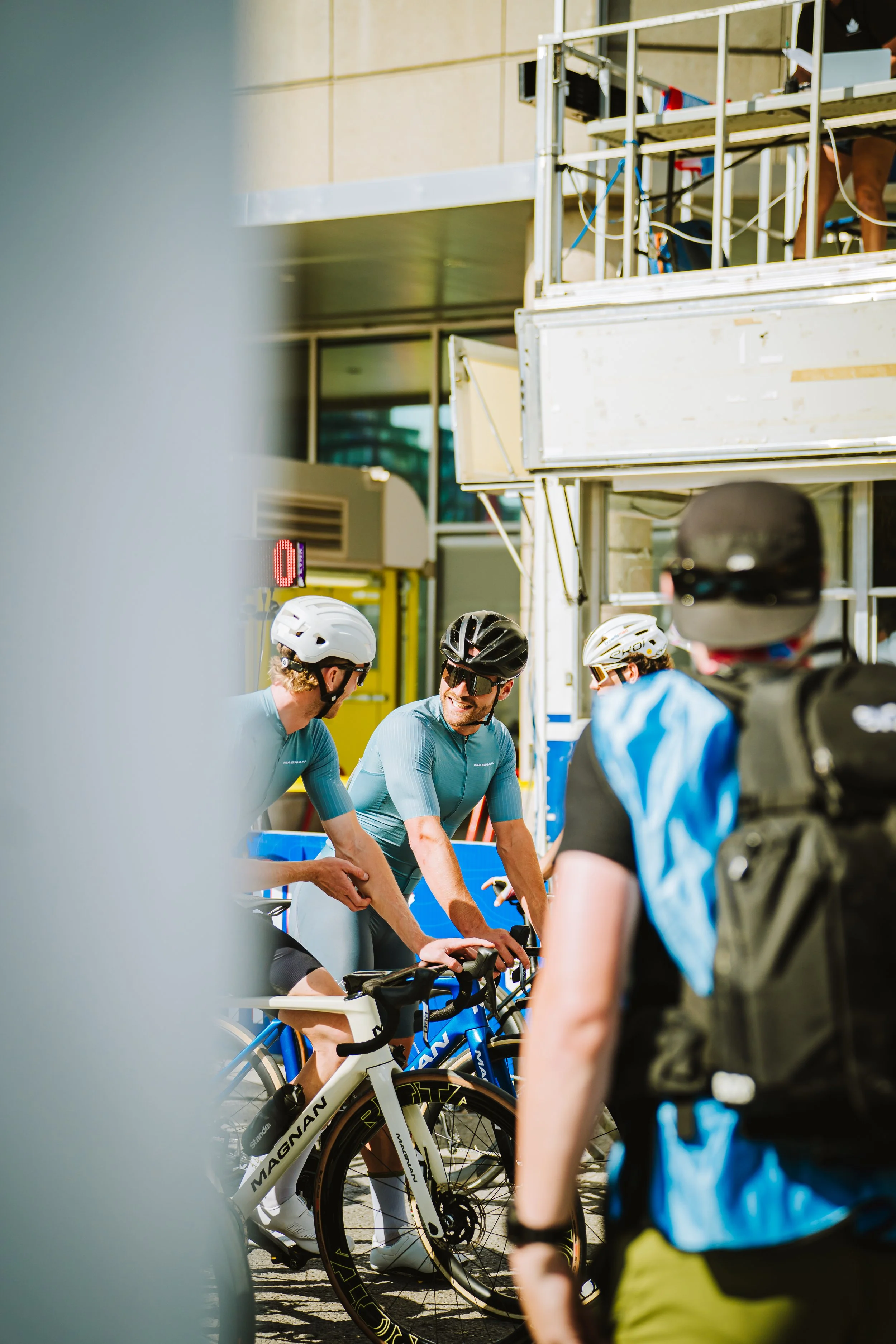 Group of cyclists in blue jerseys and helmets talking next to bikes outdoors.