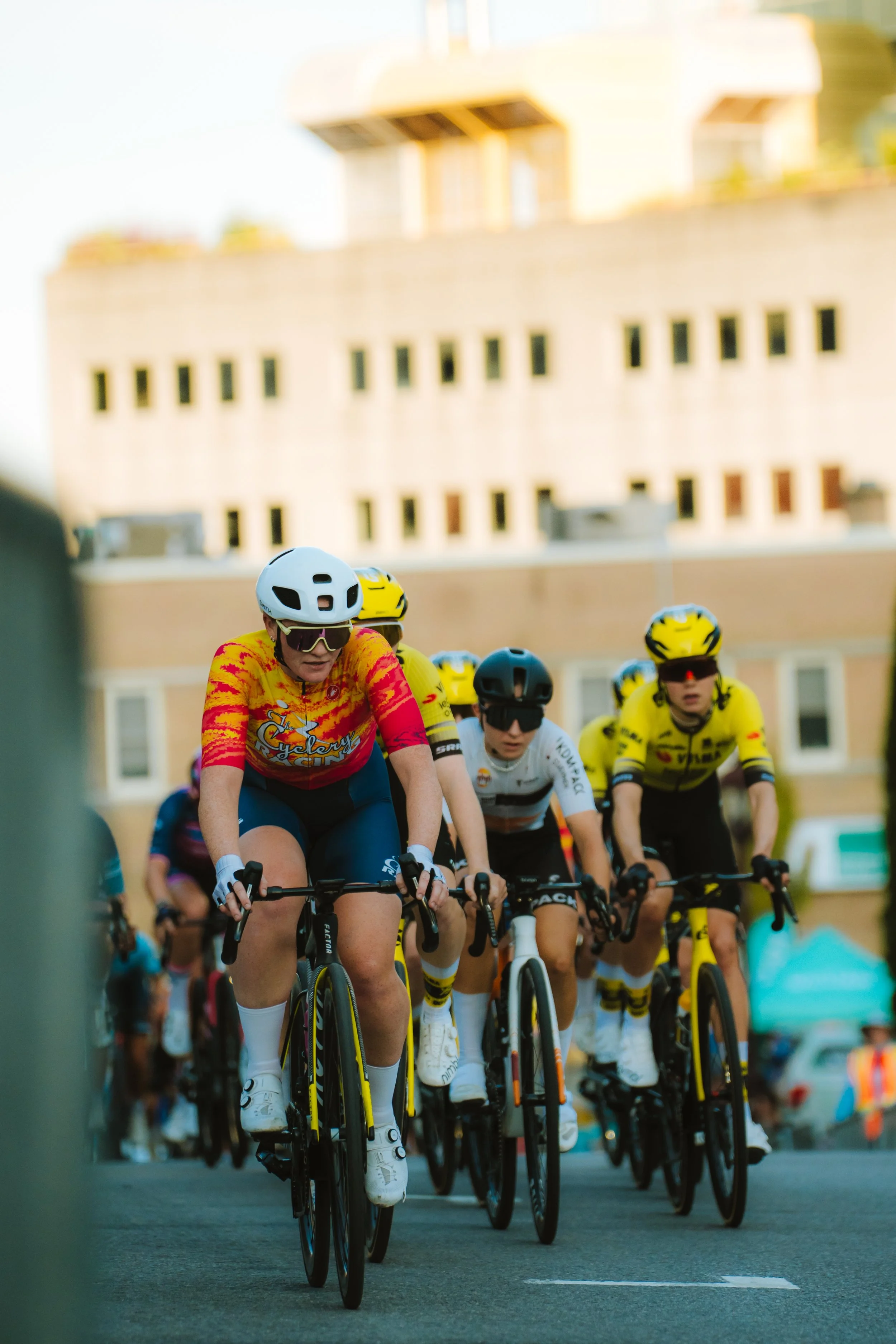A group of cyclists participating in a race on a city street, wearing helmets and colorful jerseys.