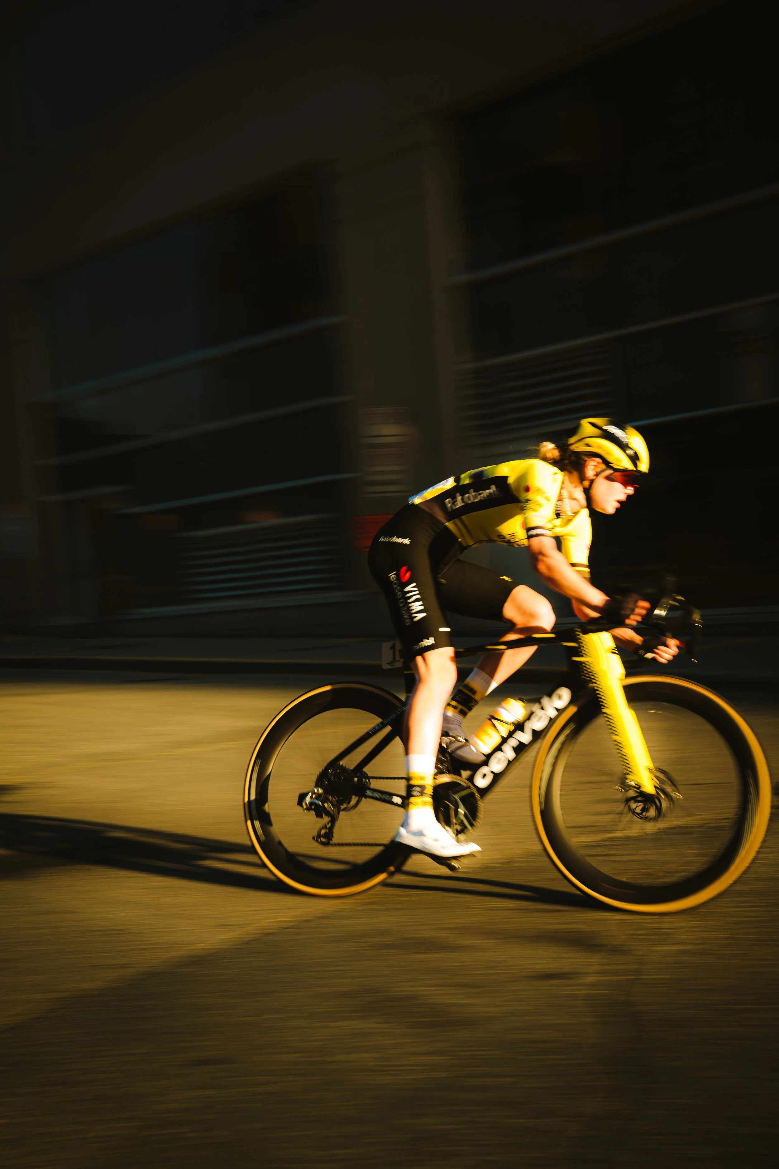A cyclist wearing a yellow and black racing outfit, helmet, and sunglasses, riding a black and yellow bike at high speed during a race, with a blurred background indicating motion.