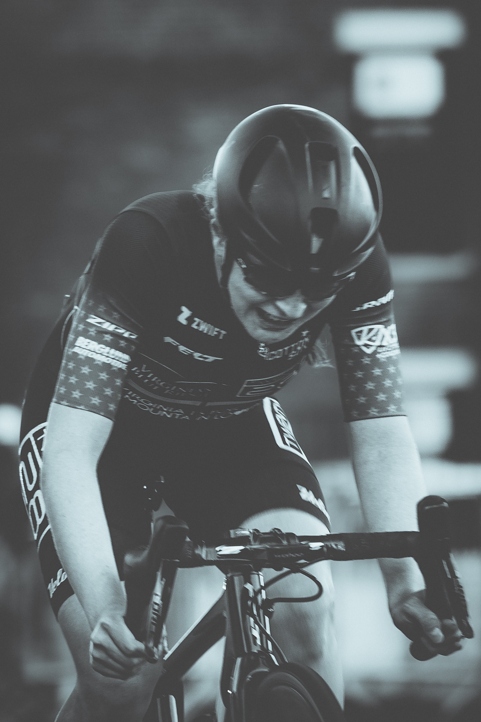 A cyclist wearing a helmet and sports gear, focused and pushing hard while riding a bike.