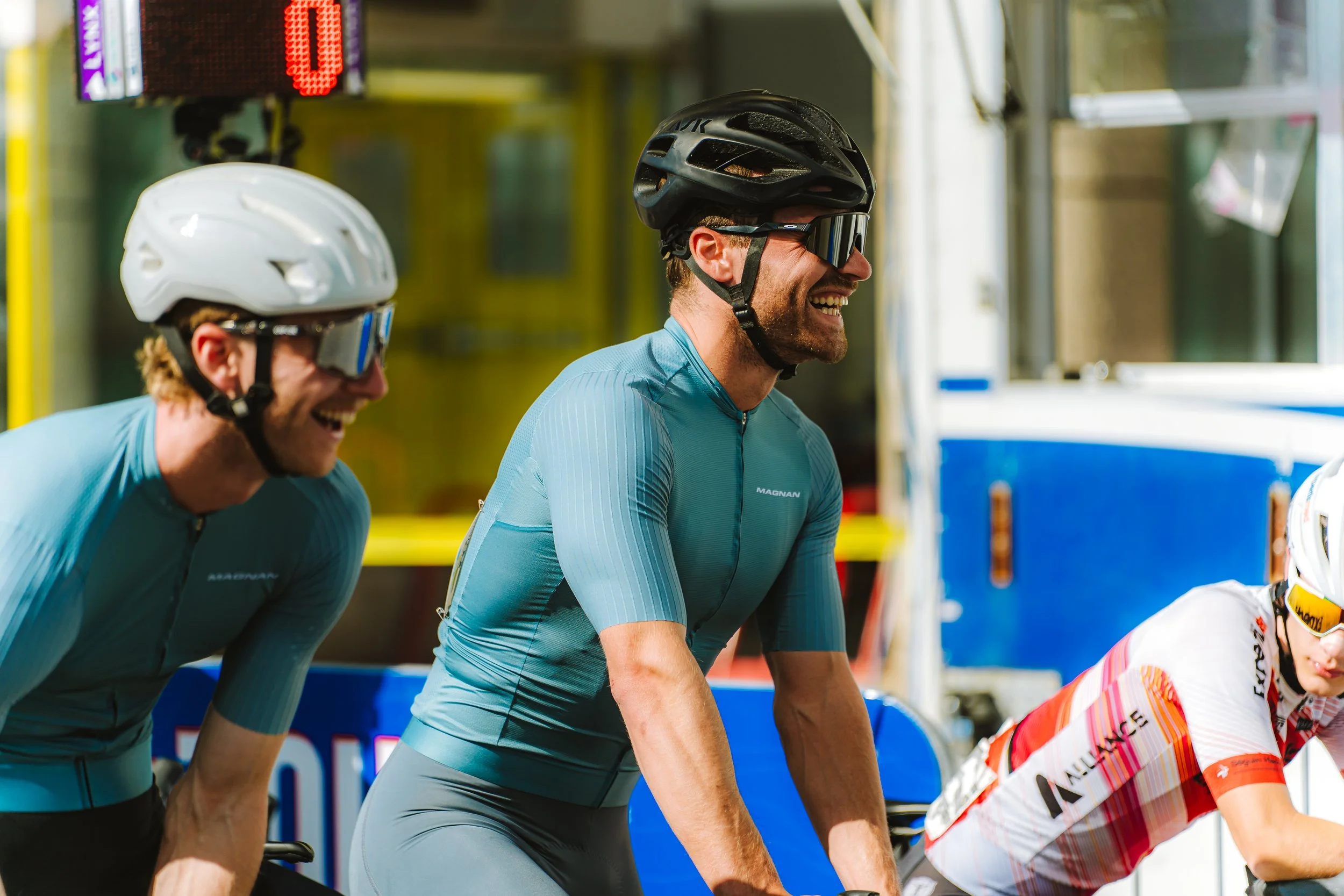 Three male cyclists in helmets and sunglasses riding on a sunny day.