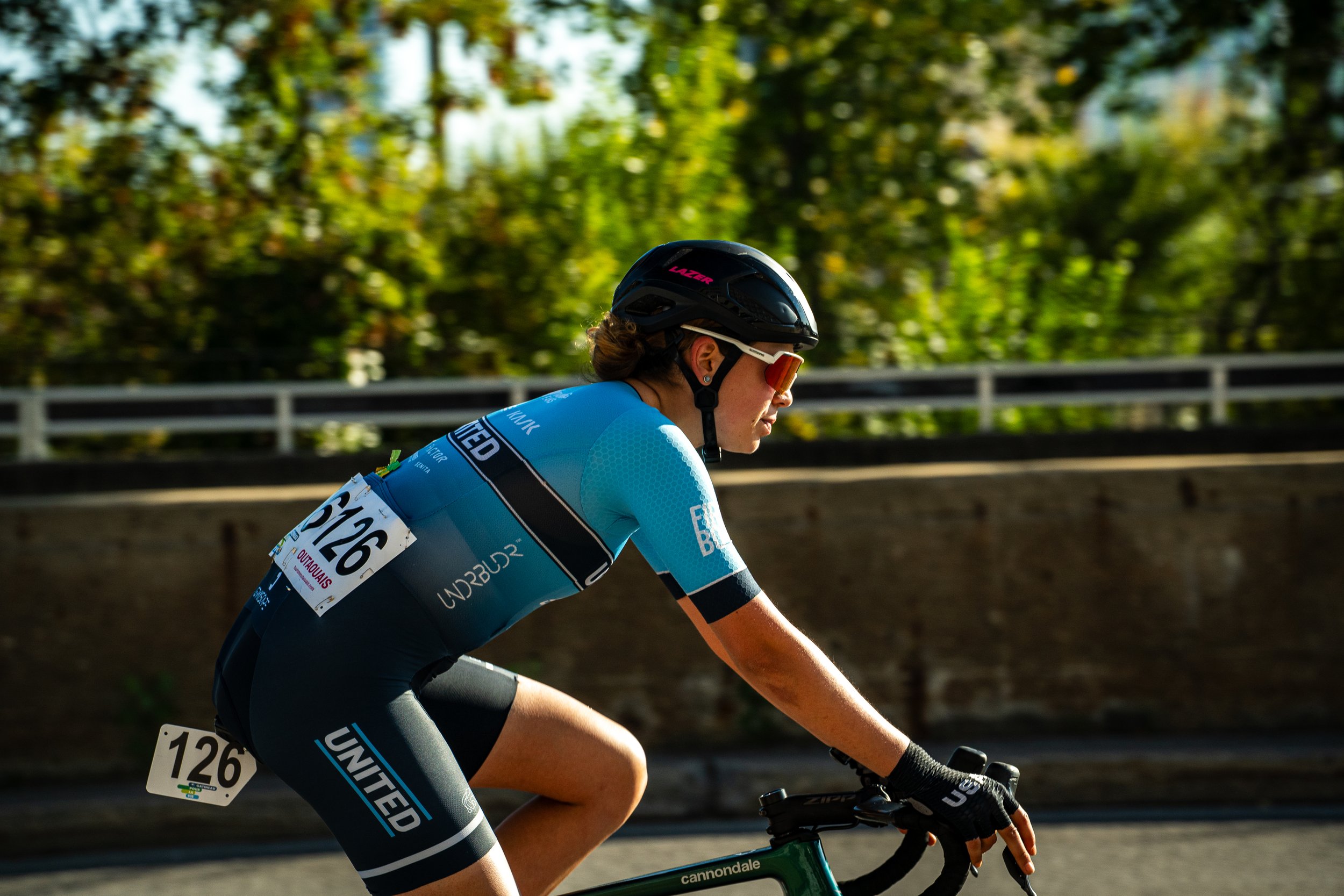 Female cyclist wearing a blue jersey, black helmet, riding a green Cannondale bike during a race.