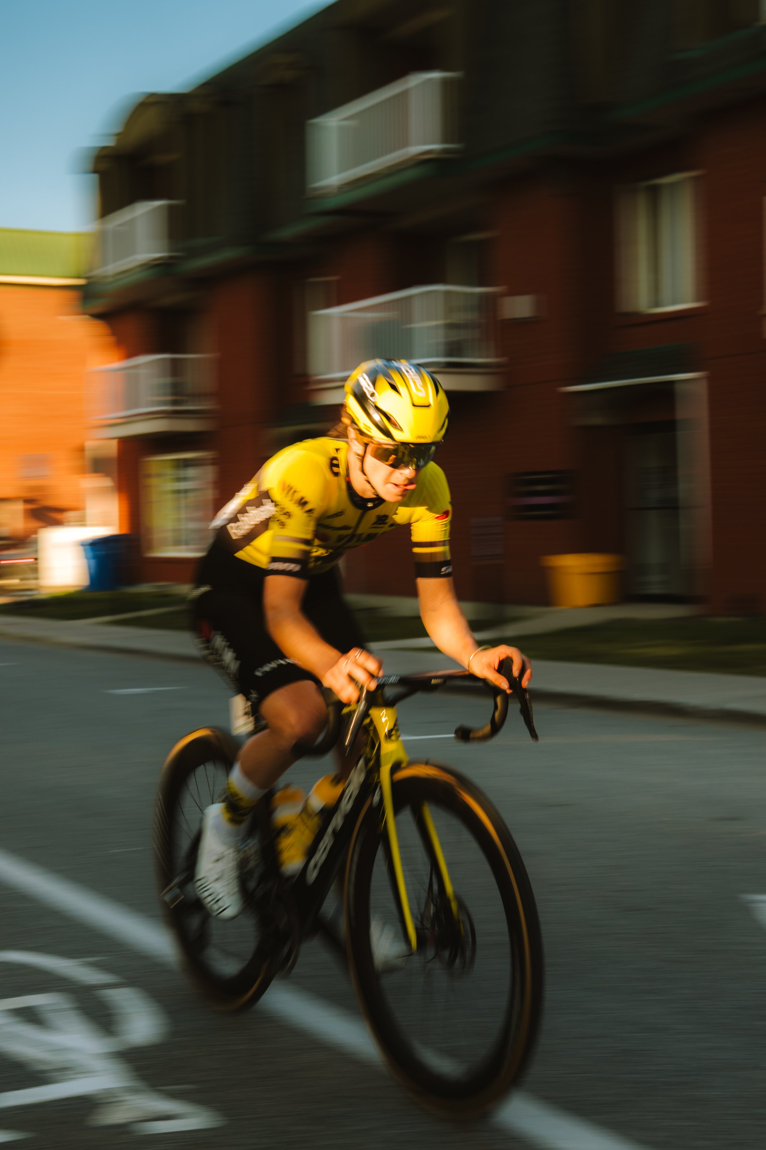 A cyclist wearing a yellow helmet and jersey riding a bicycle on a city street during sunset.