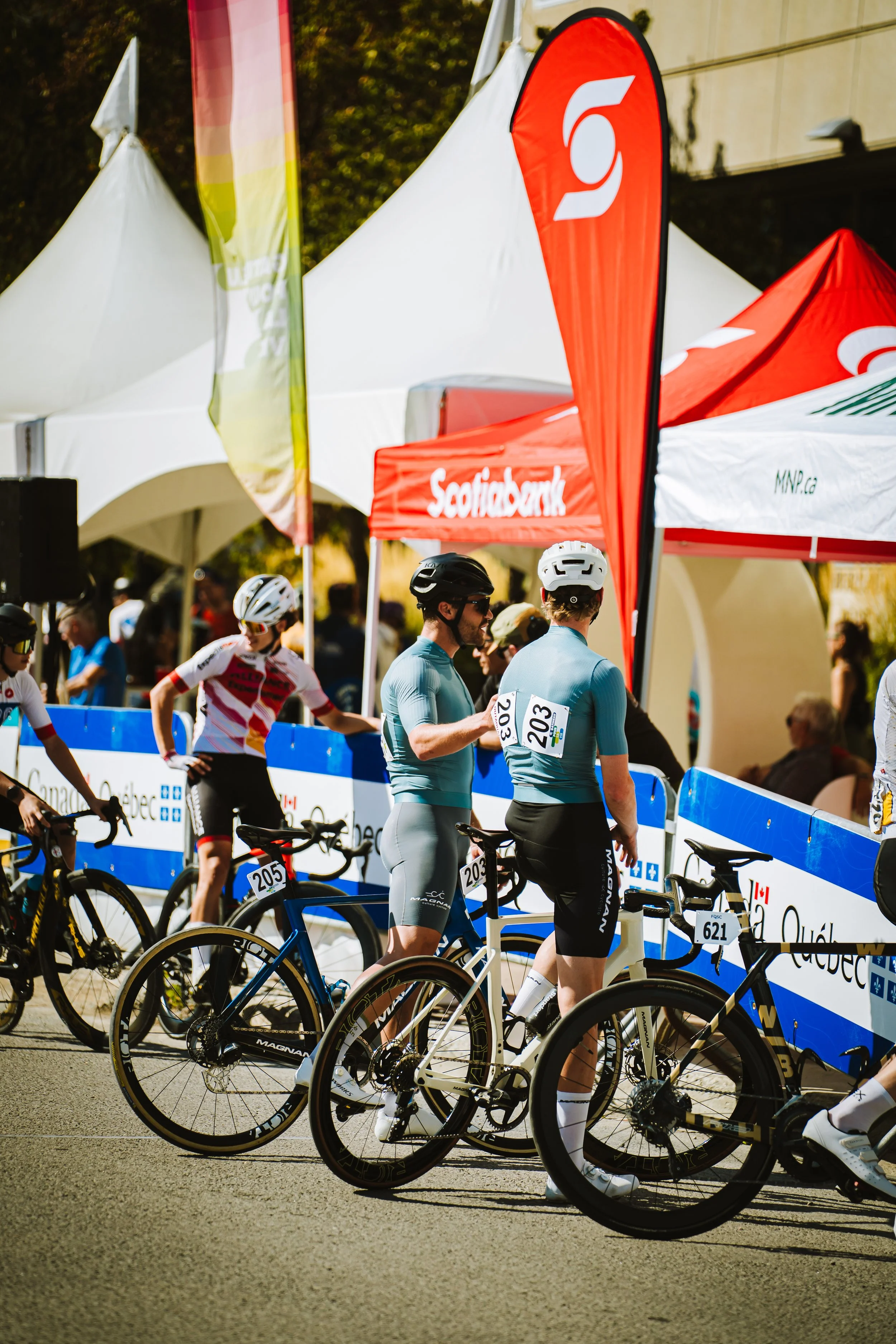 Cyclists preparing at a race with tents and flags in the background.
